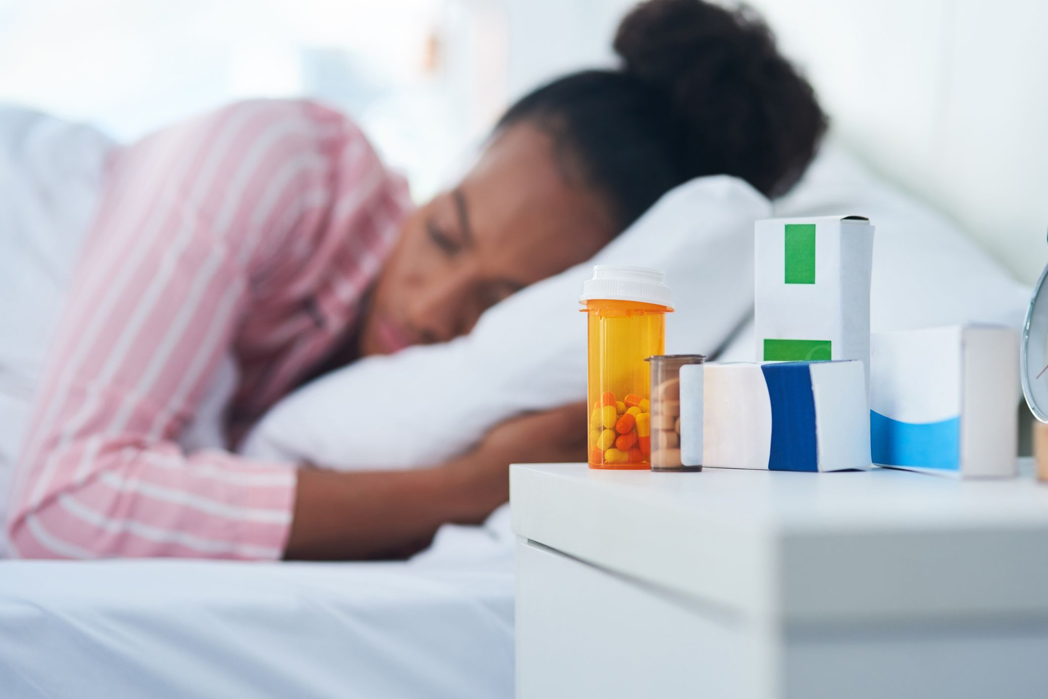sleeping pills, young woman sleeping in bed with her medication on the dresser at home