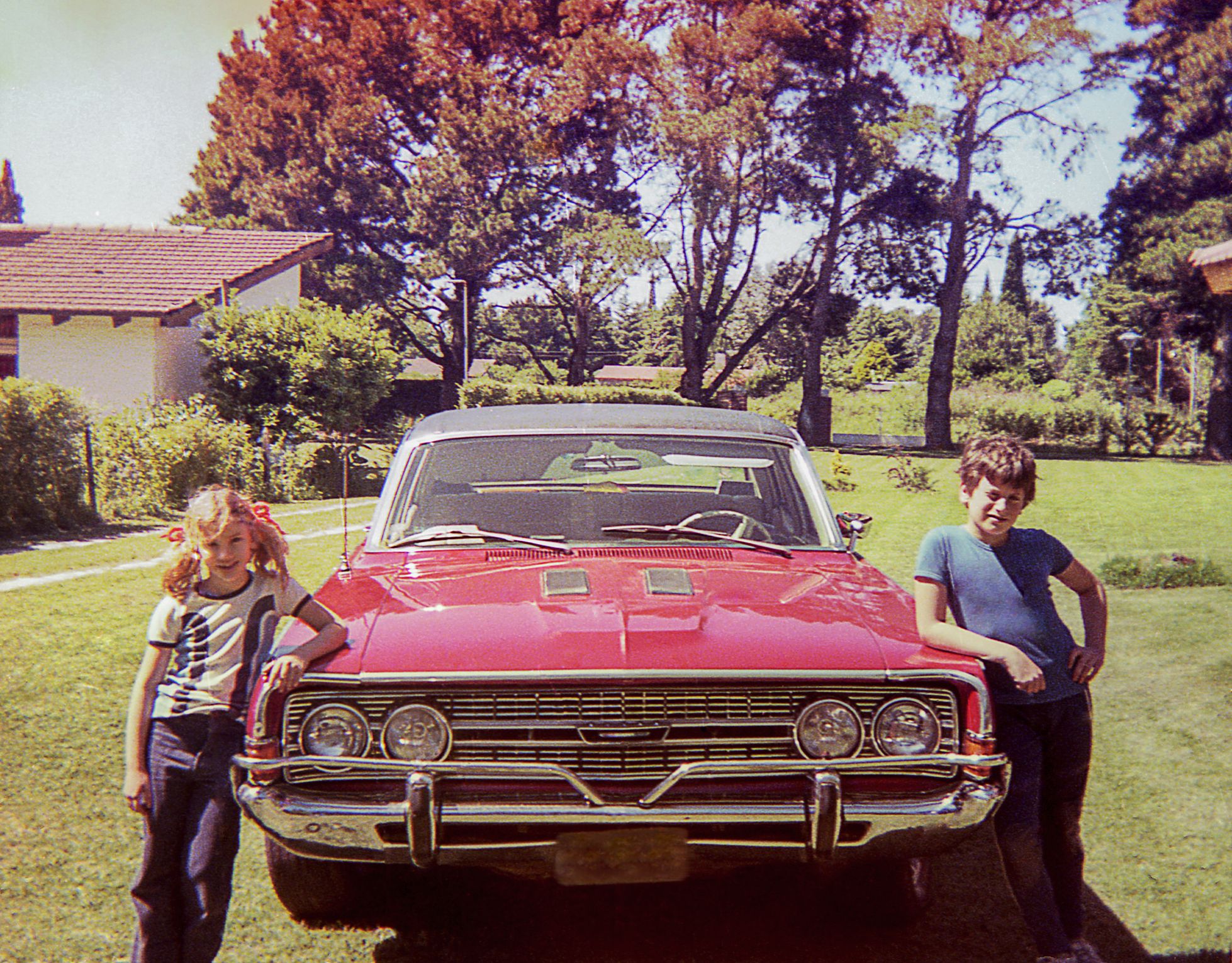 Vintage photo of a cute a couple of children posing beside a big vintage car.