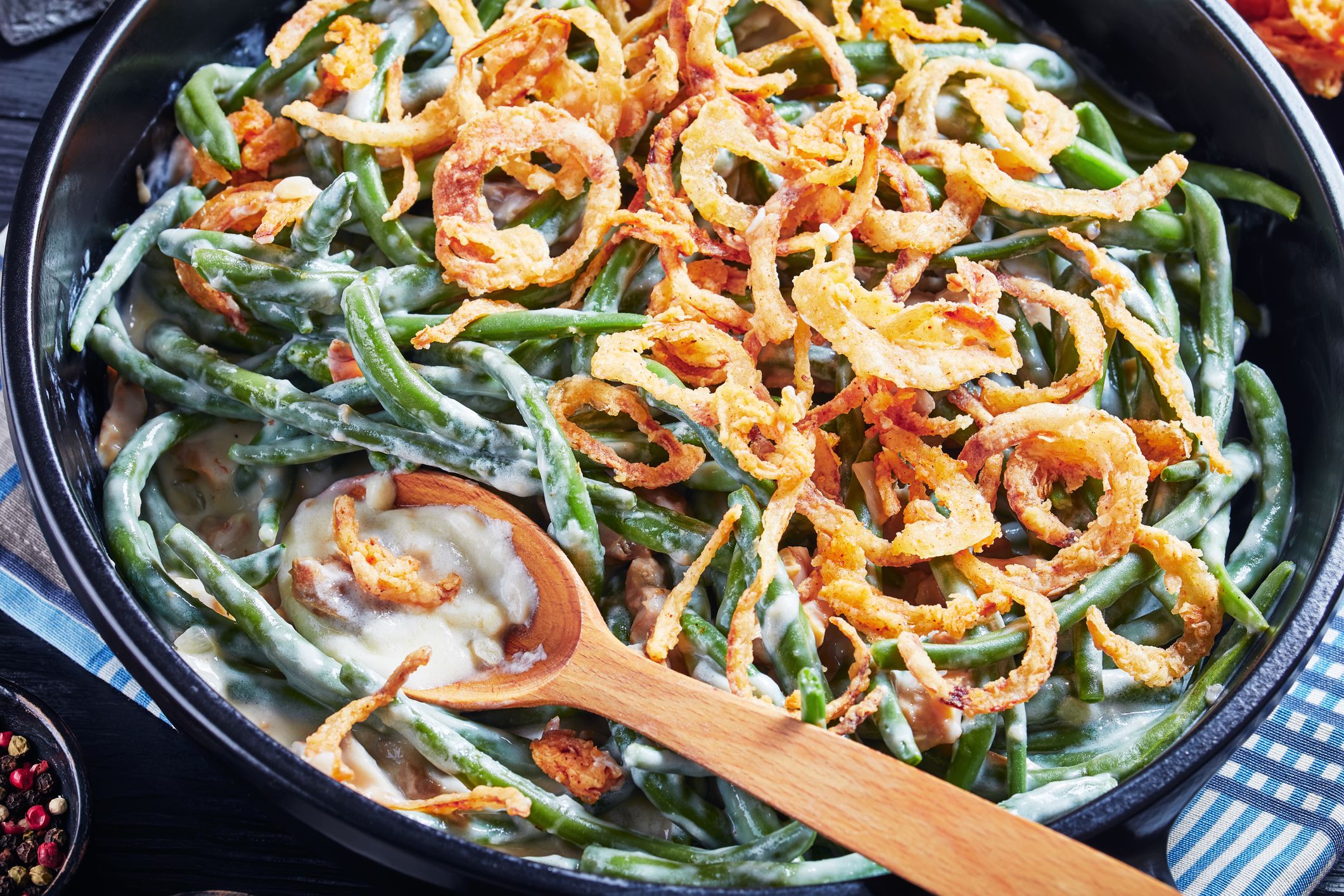 close-up of Green Bean Casserole topped with crispy fried onions in a black dish with spoon, american cuisine, view from above