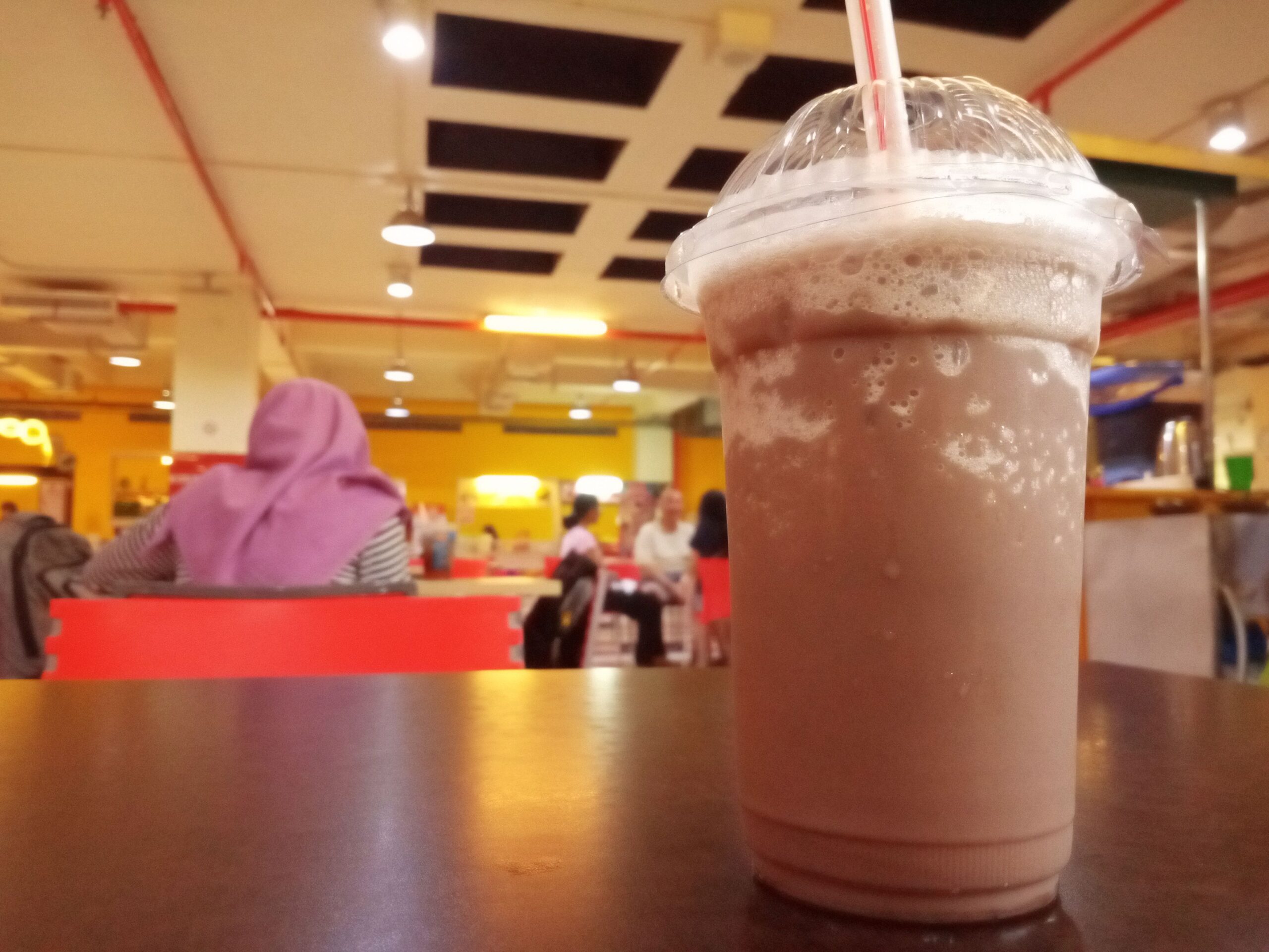 Chocolate flavor beverage in plastic cups on the table in the mall. Selective focus with many people background.