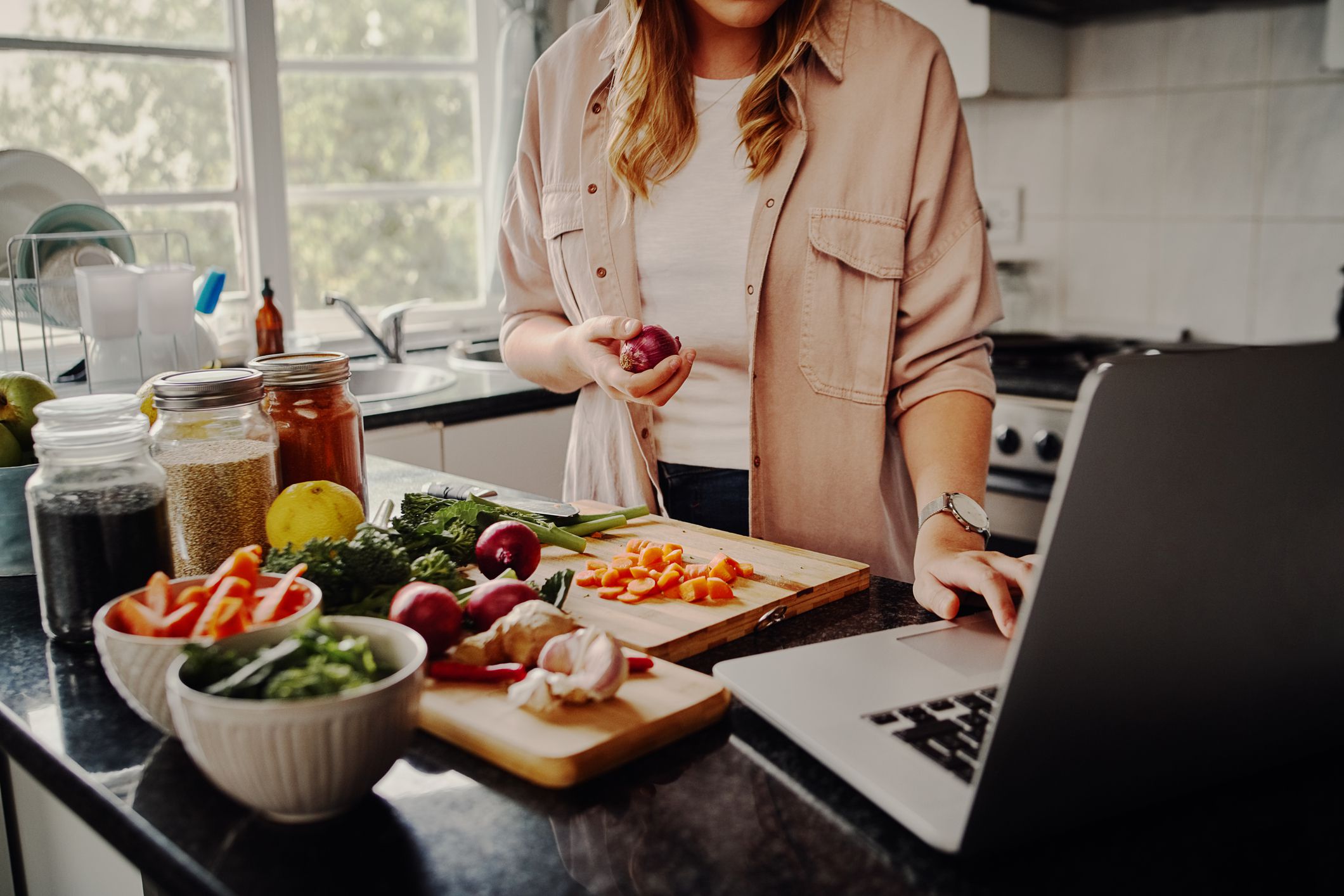 Young female blogger searching online browsing for recipes to prepare salad of fresh vegetables and post on social media in vlog - new fun hobby during isolation