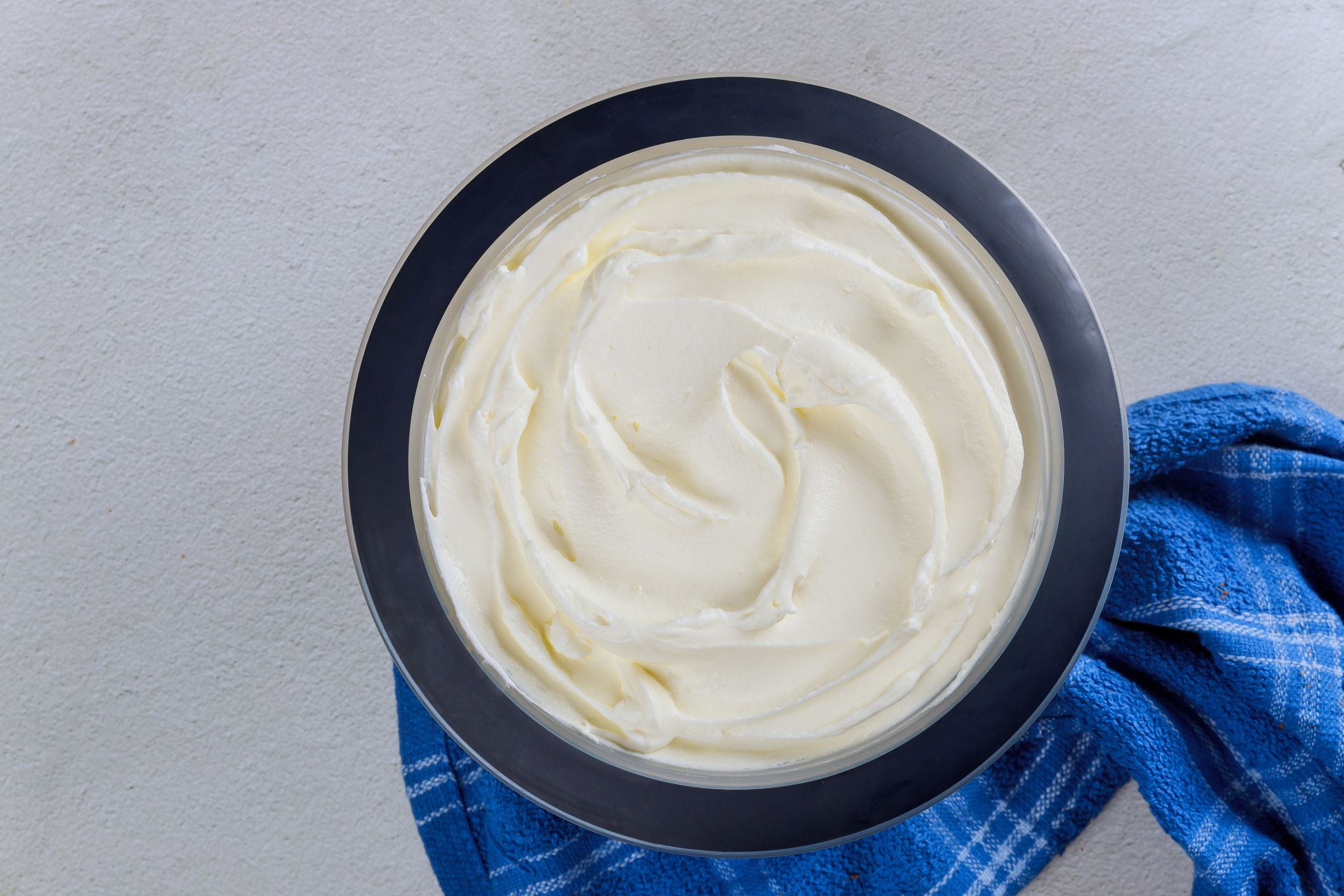 Homemade vanilla whipped cream in a bowl with blue towel. Top view.