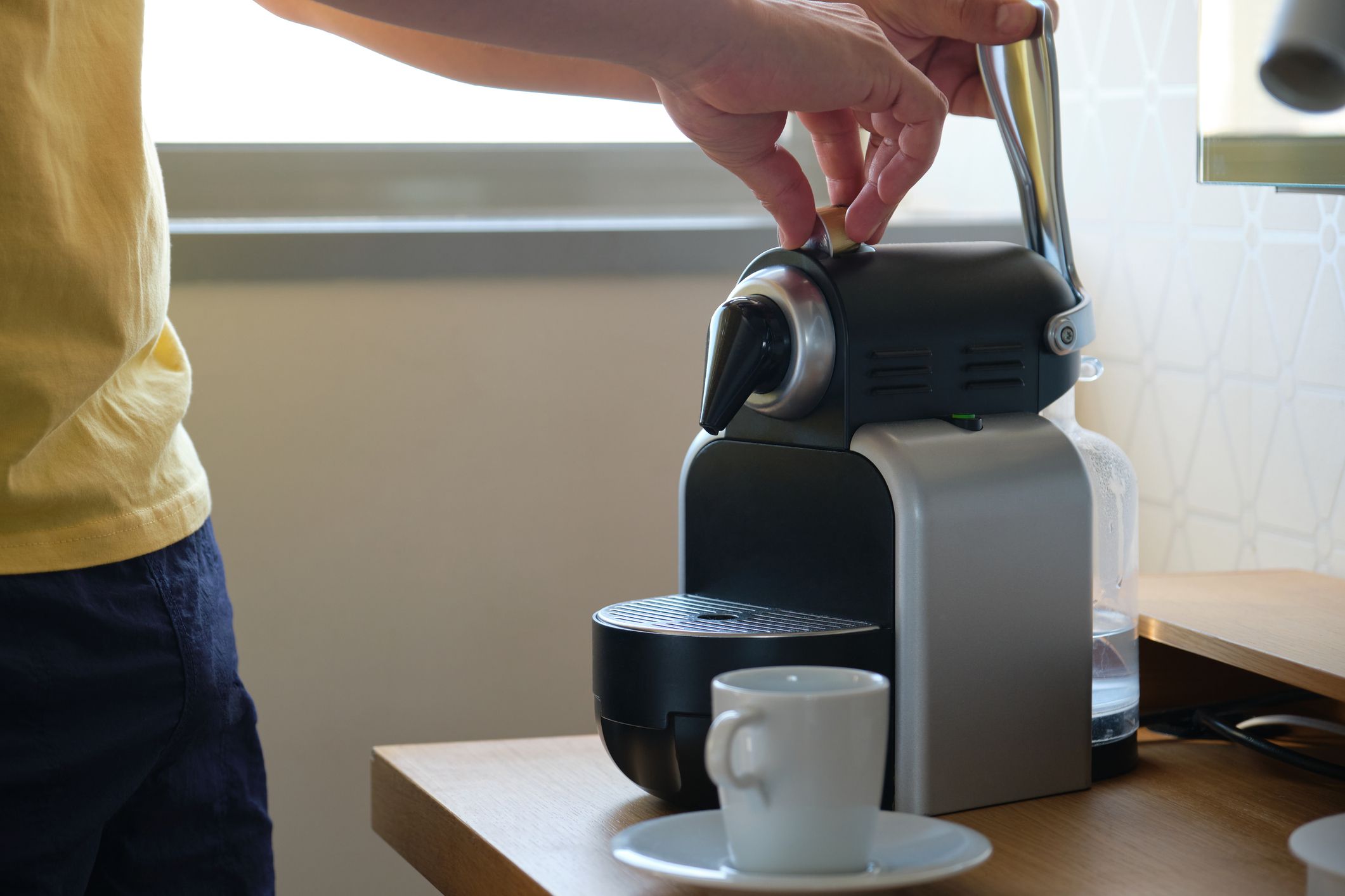 Unrecognizable man preparing coffee in a coffee machine with capsules in a hotel room.
