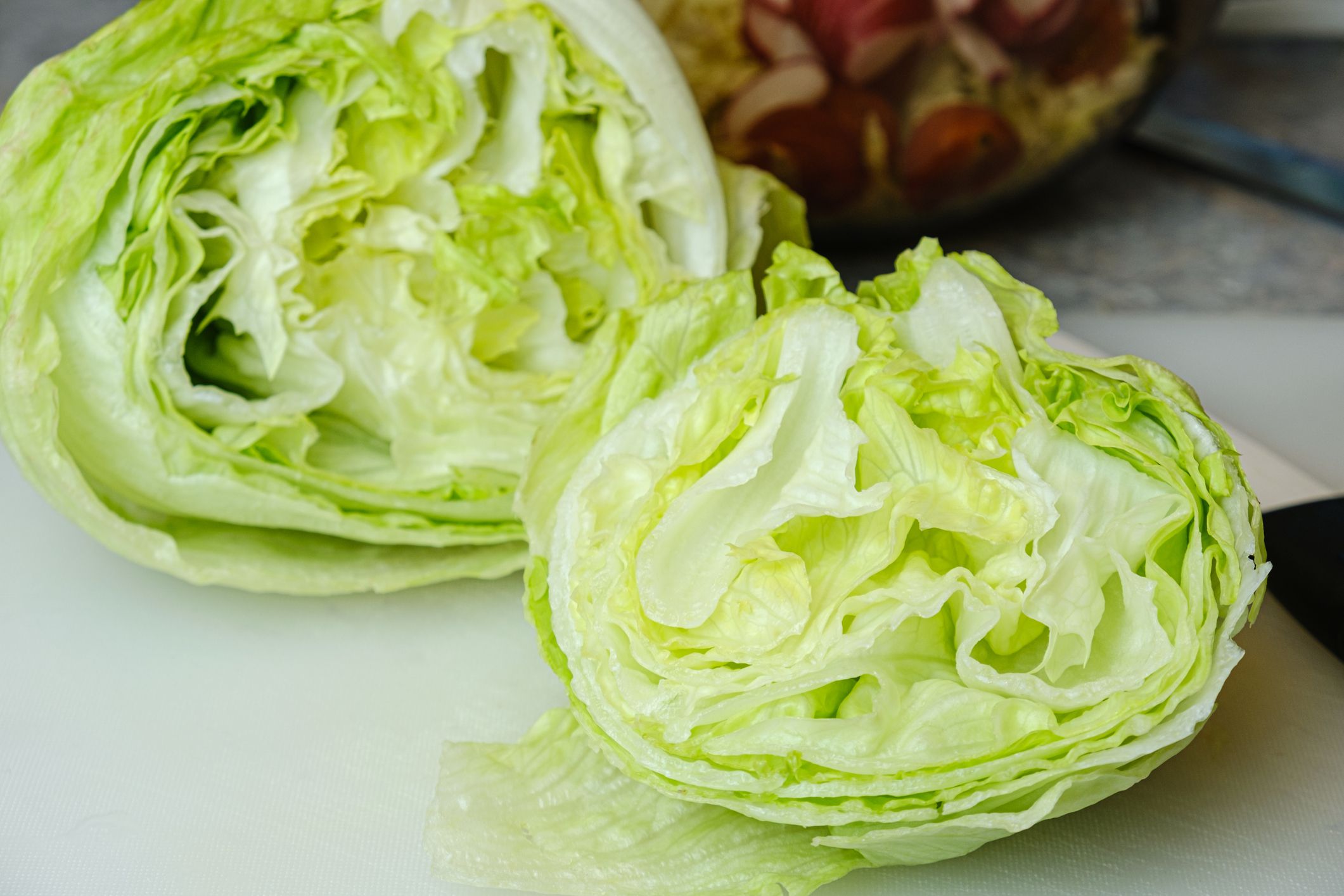 Cut bulb of fresh iceberg lettuce also known as crisphead lettuce on a cutting board. Selective focus, blurred background.