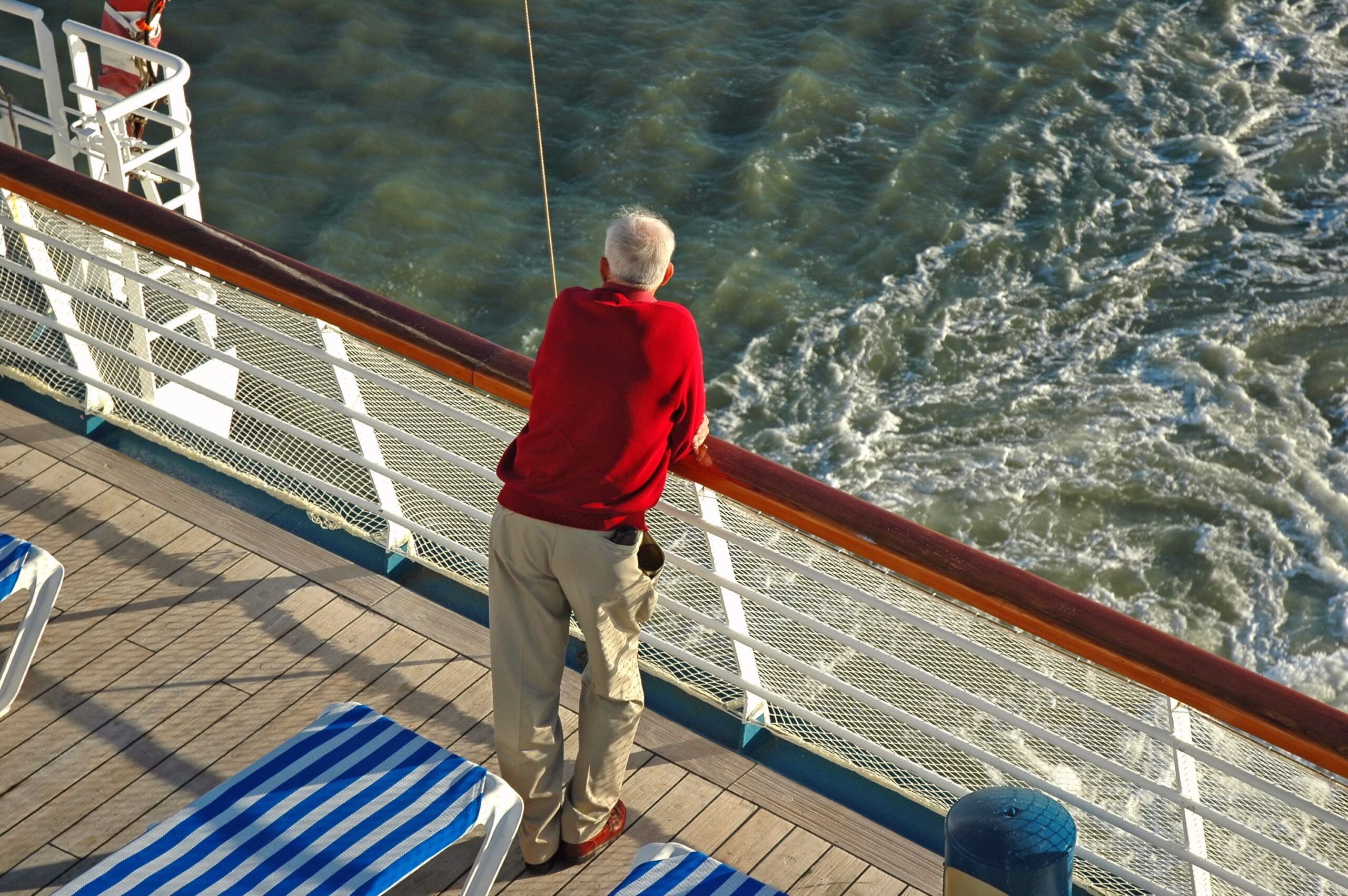 A senior stands on the rear deck of a cruise ship and overlooks the ocean
