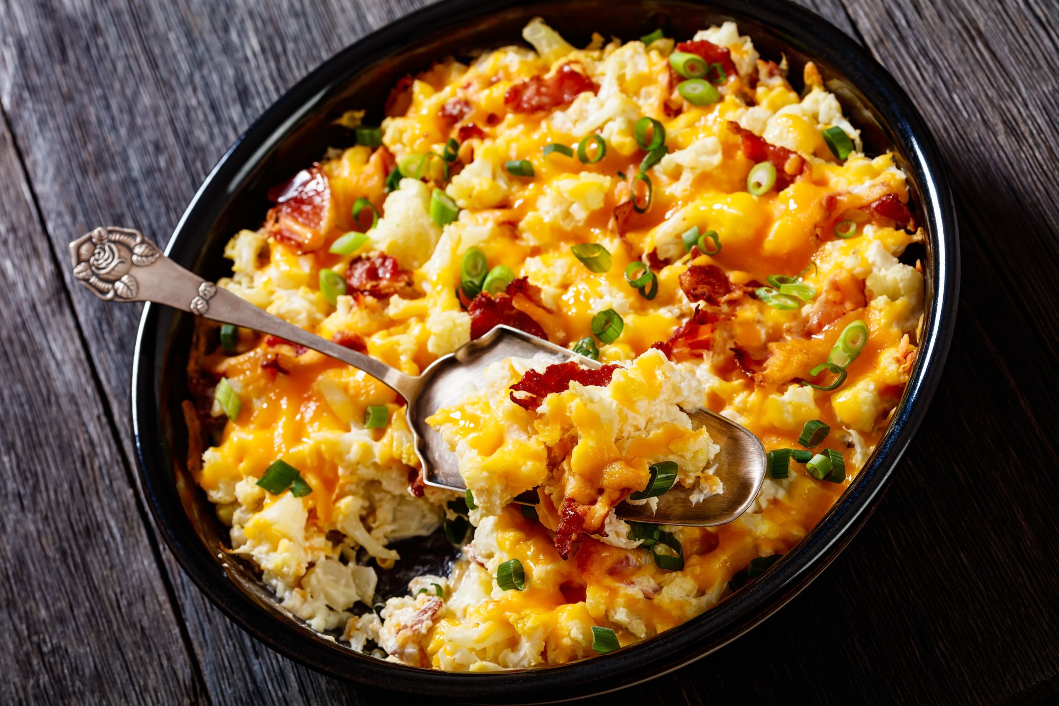 cauliflower bacon cheese casserole in baking dish on dark wood table, close-up