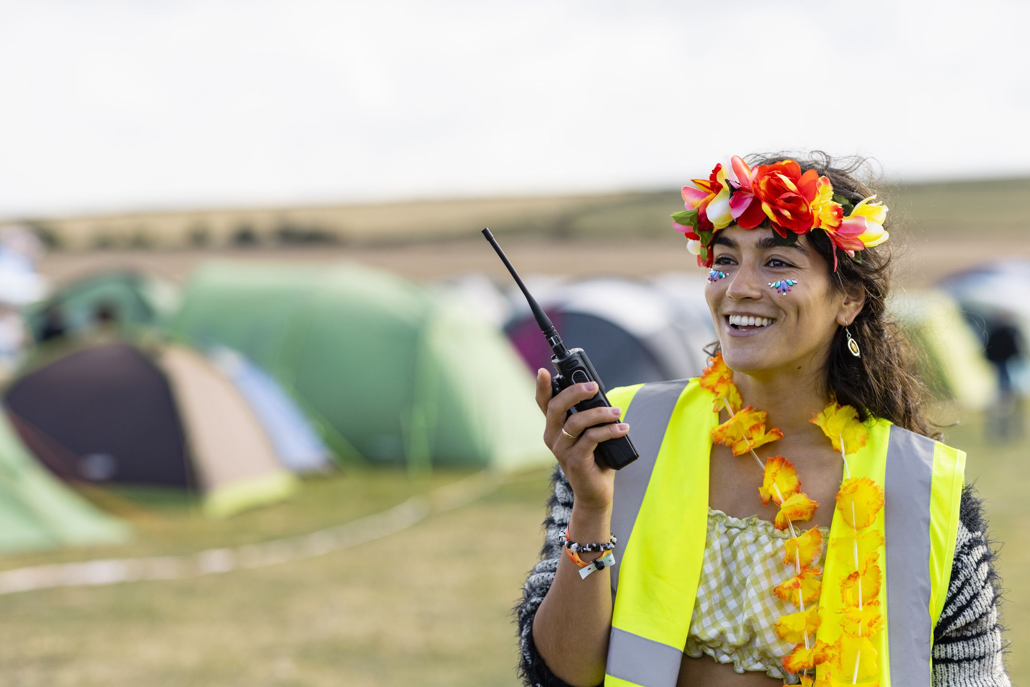 A volunteer wearing a reflective vest and working at a festival in Lindisfarne, North East England. She is talking to someone using a walkie talkie while smiling.