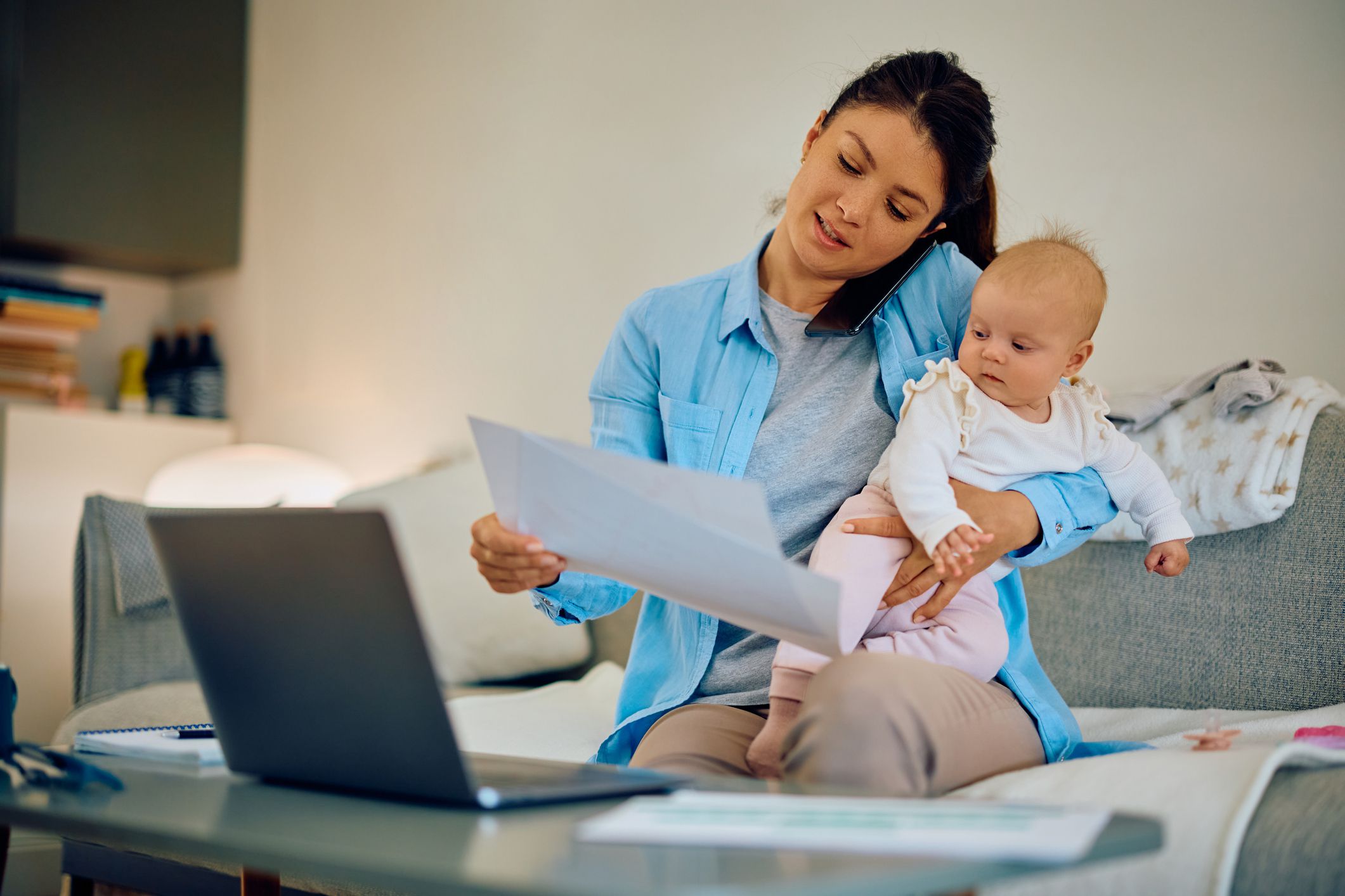 Busy mother talking on mobile phone while analyzing reports and babysitting her daughter at home.