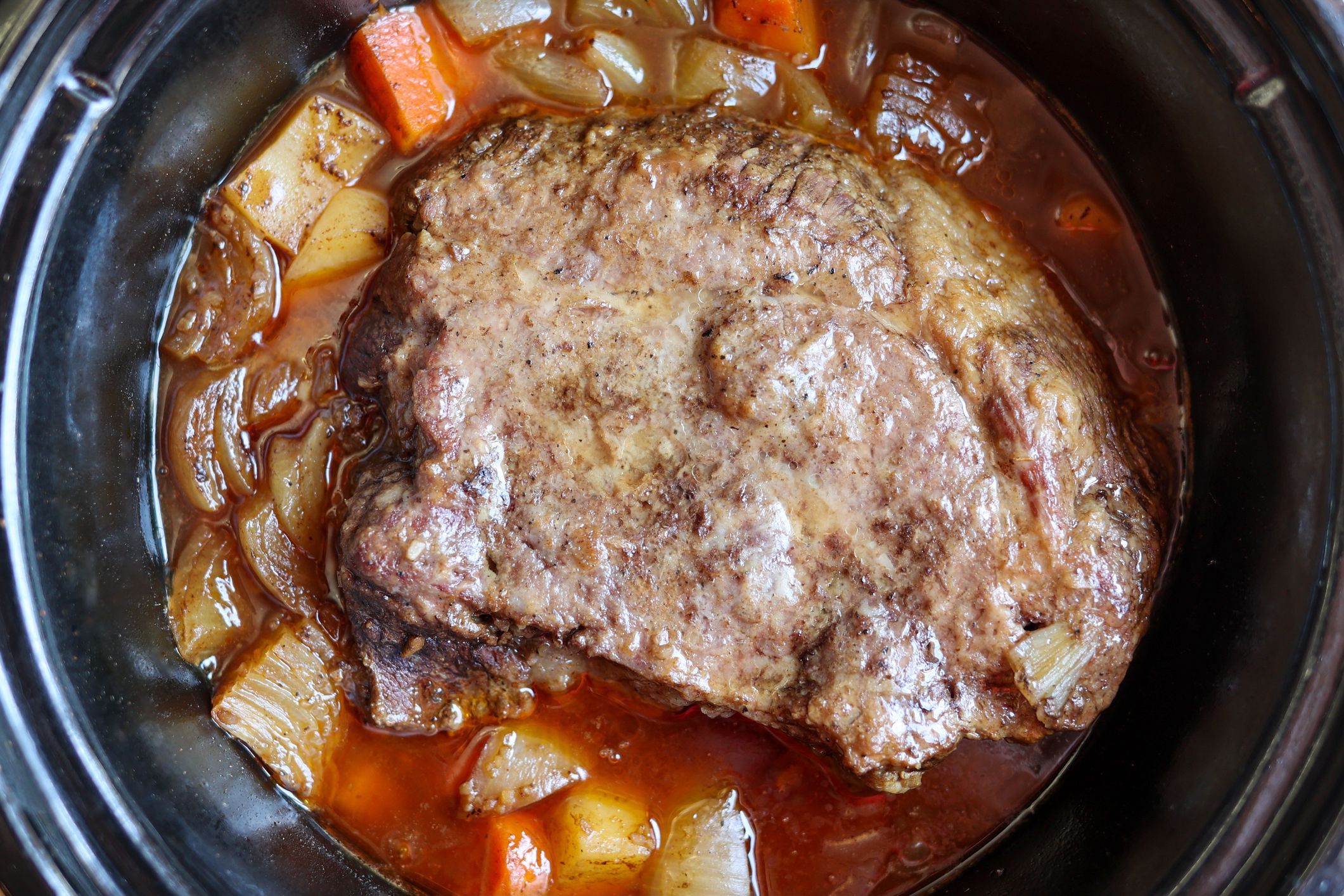 A homemade pot roast cooking inside of a crockpot