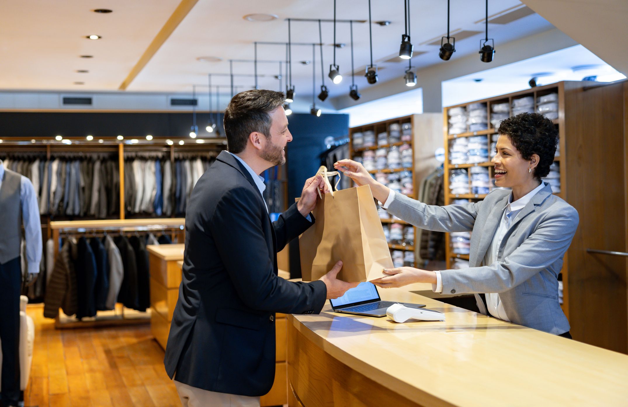 Latin American man shopping at a clothing store with the help of a retail clerk and receiving a bag