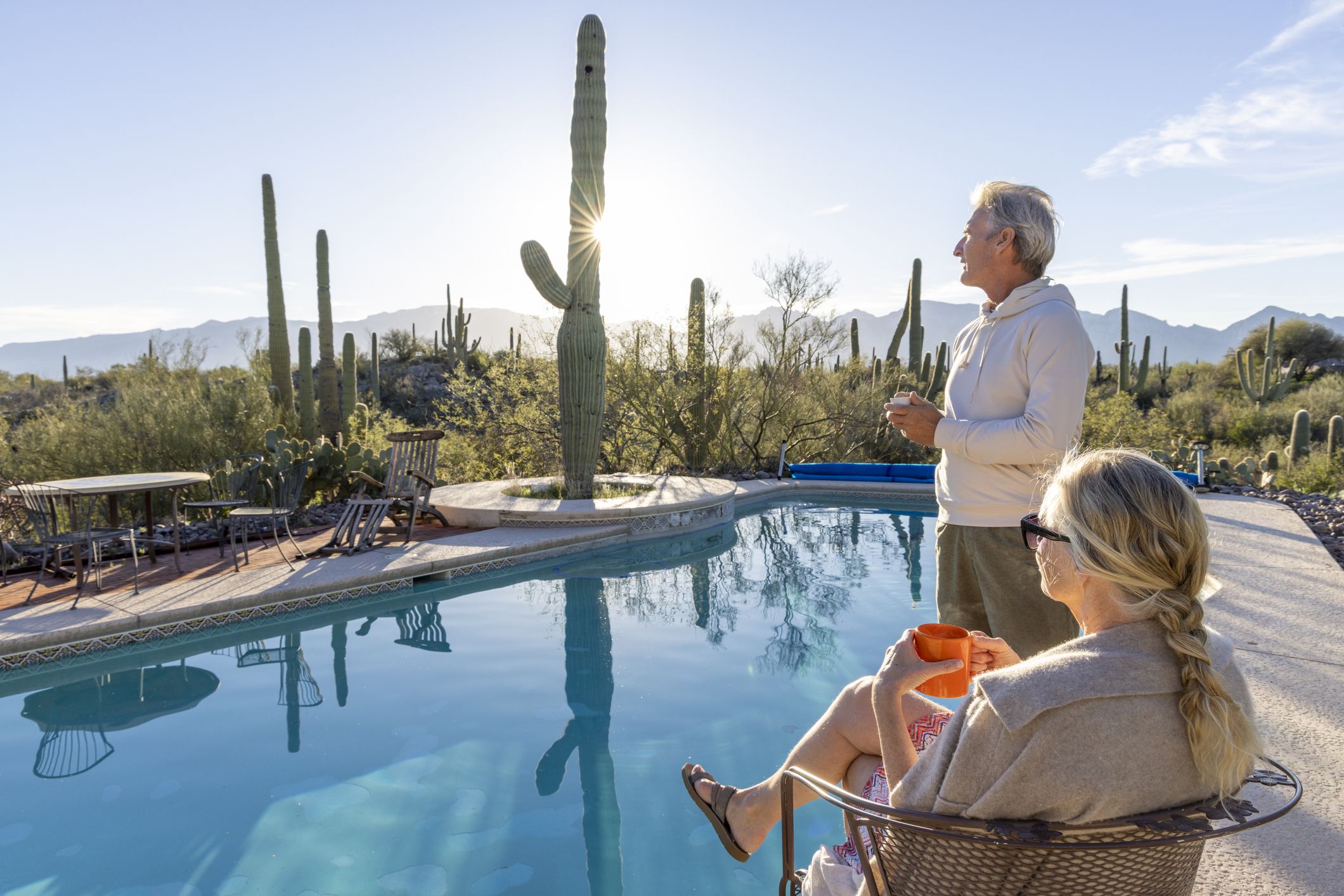 Mature couple relax at desert swimming pool and enjoy hot beverage