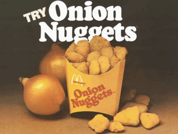 A McDonald&rsquo;s container filled with onion nuggets, surrounded by whole onions and loose nuggets, with large text above reading &ldquo;Try Onion Nuggets.&rdquo;