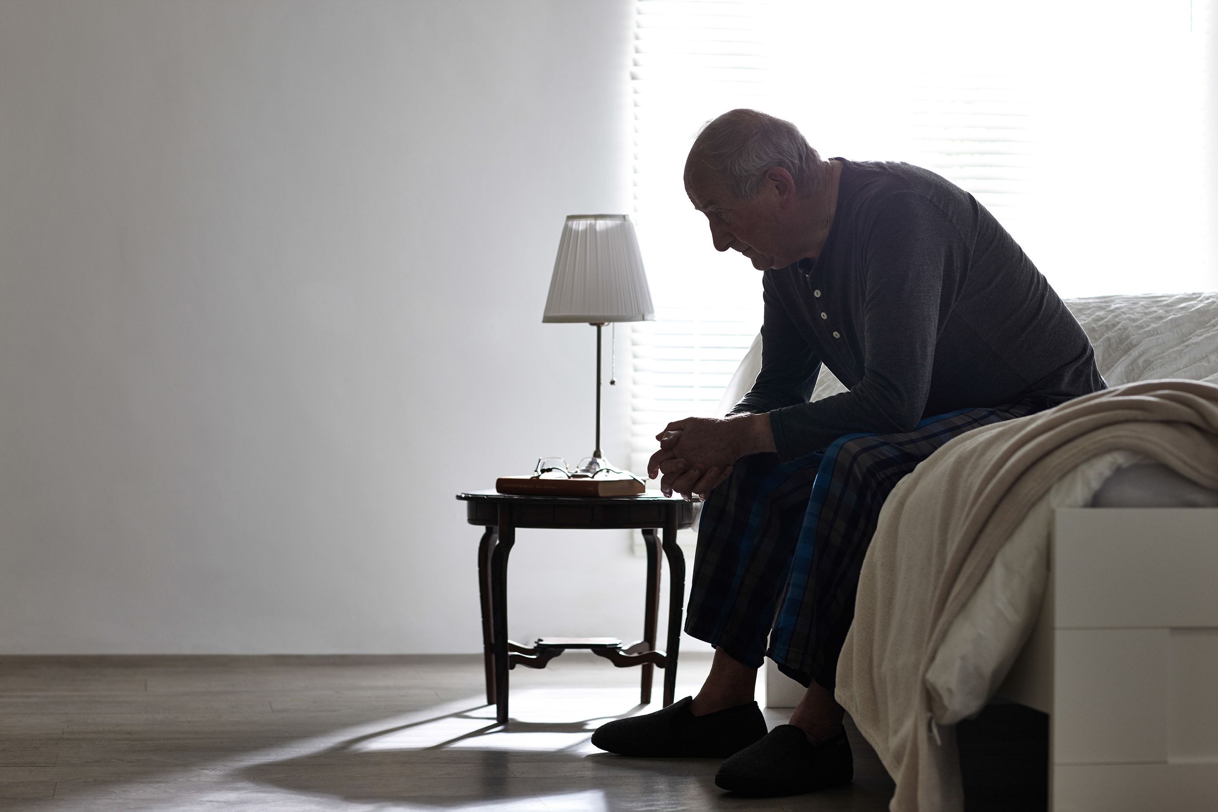 elderly man sitting on bed looking serious in darkness