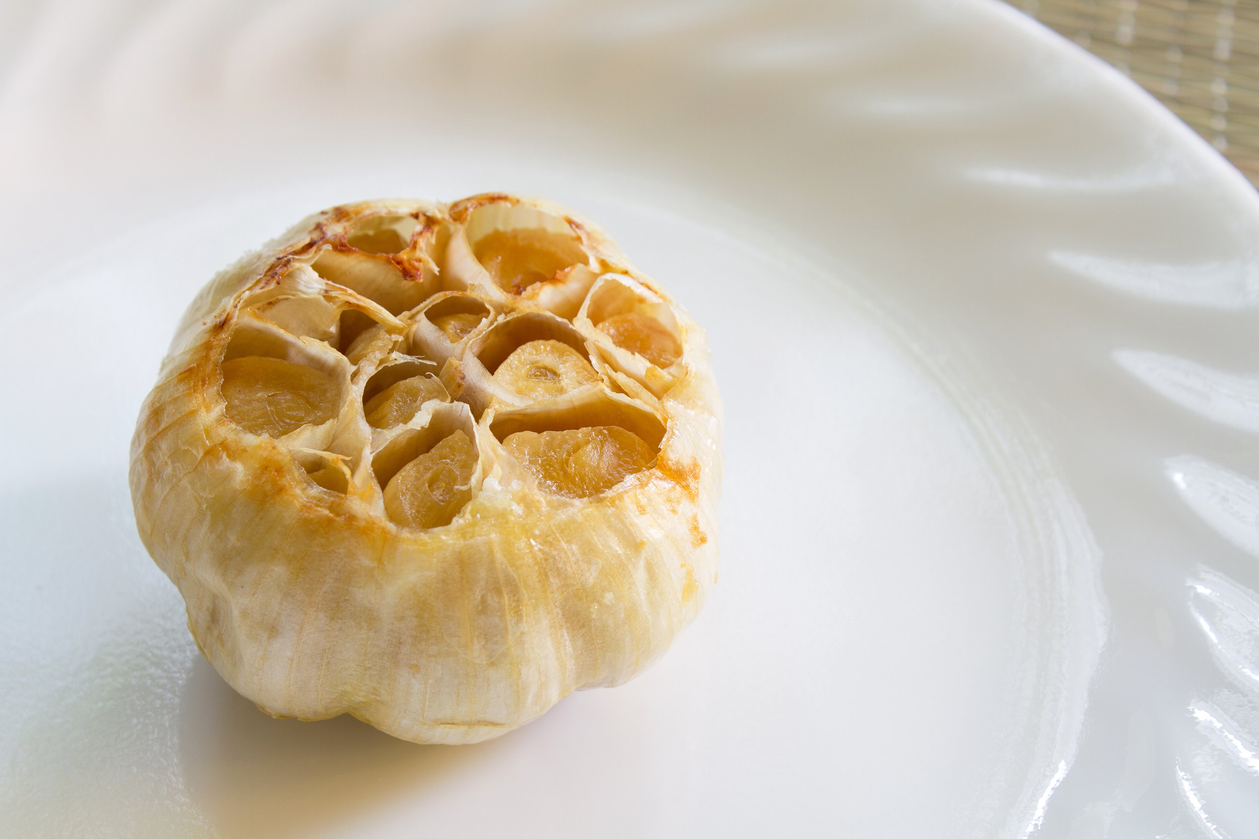 Whole bulb of roasted garlic on a white plate
