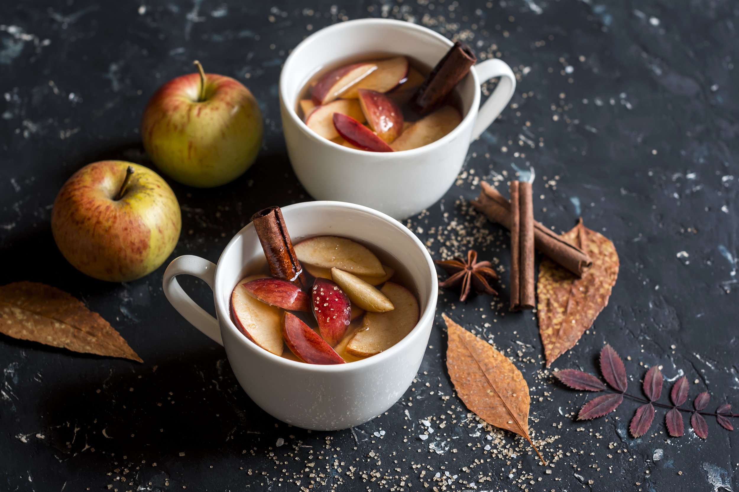 Hot mulled cider in white mugs with apple and cinnamon decorations in background