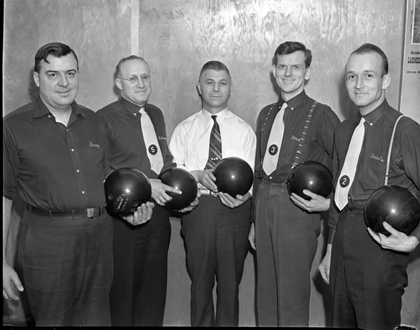 Group of five middle aged white men holding bowling balls.