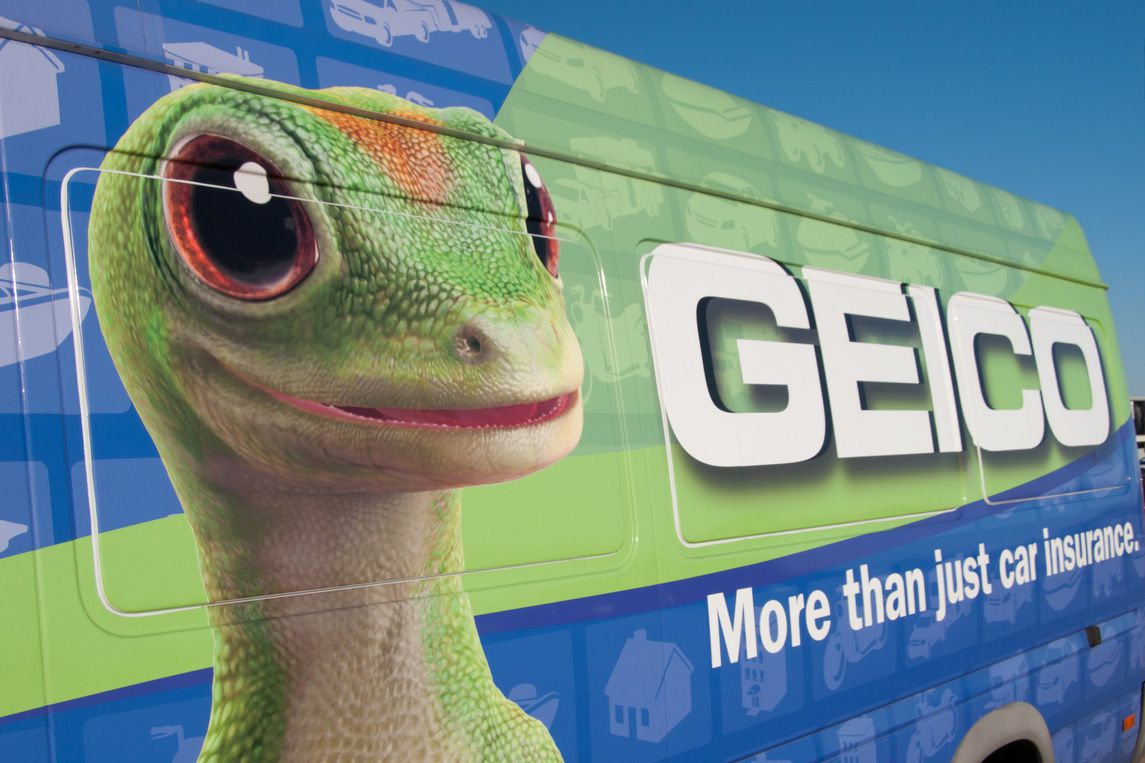 A GEICO van features a large image of the GEICO gecko mascot and the text "GEICO" and "More than just car insurance" on its side against a blue background.