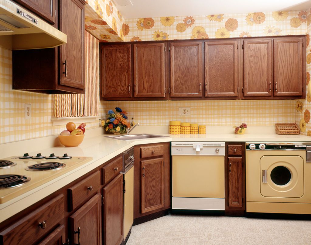 1970s KITCHEN INTERIOR WITH YELLOW APPLIANCES WOOD CABINETS AND SUNFLOWER FLORAL PRINT WALLPAPER