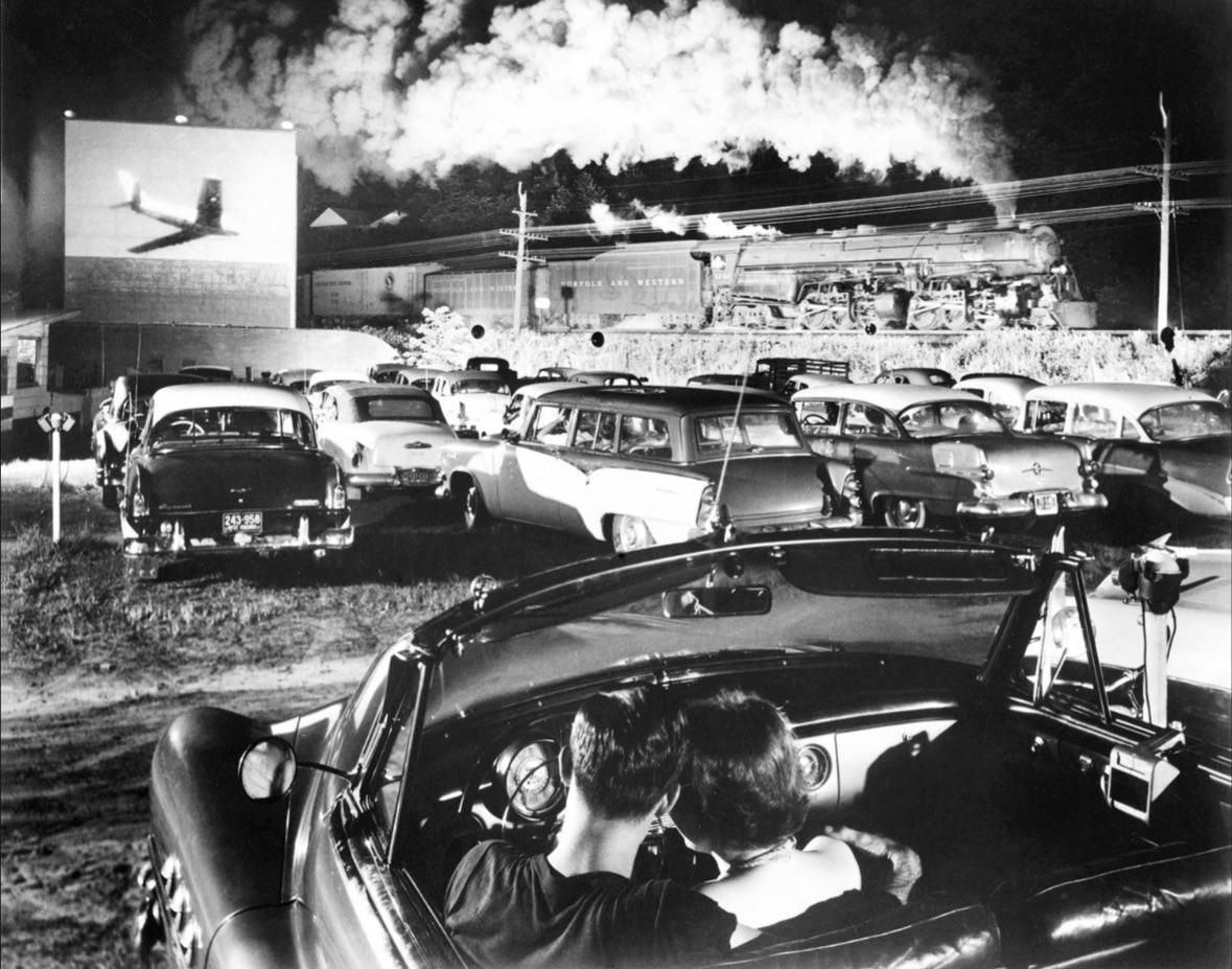 Norfolk and Western Railway steam train passing a drive-in movie theater at night. Iaeger, West Virginia, USA. 1956