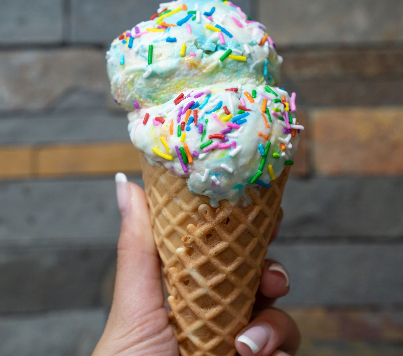 Womans hand holding waffle cone with birthday cake ice cream
