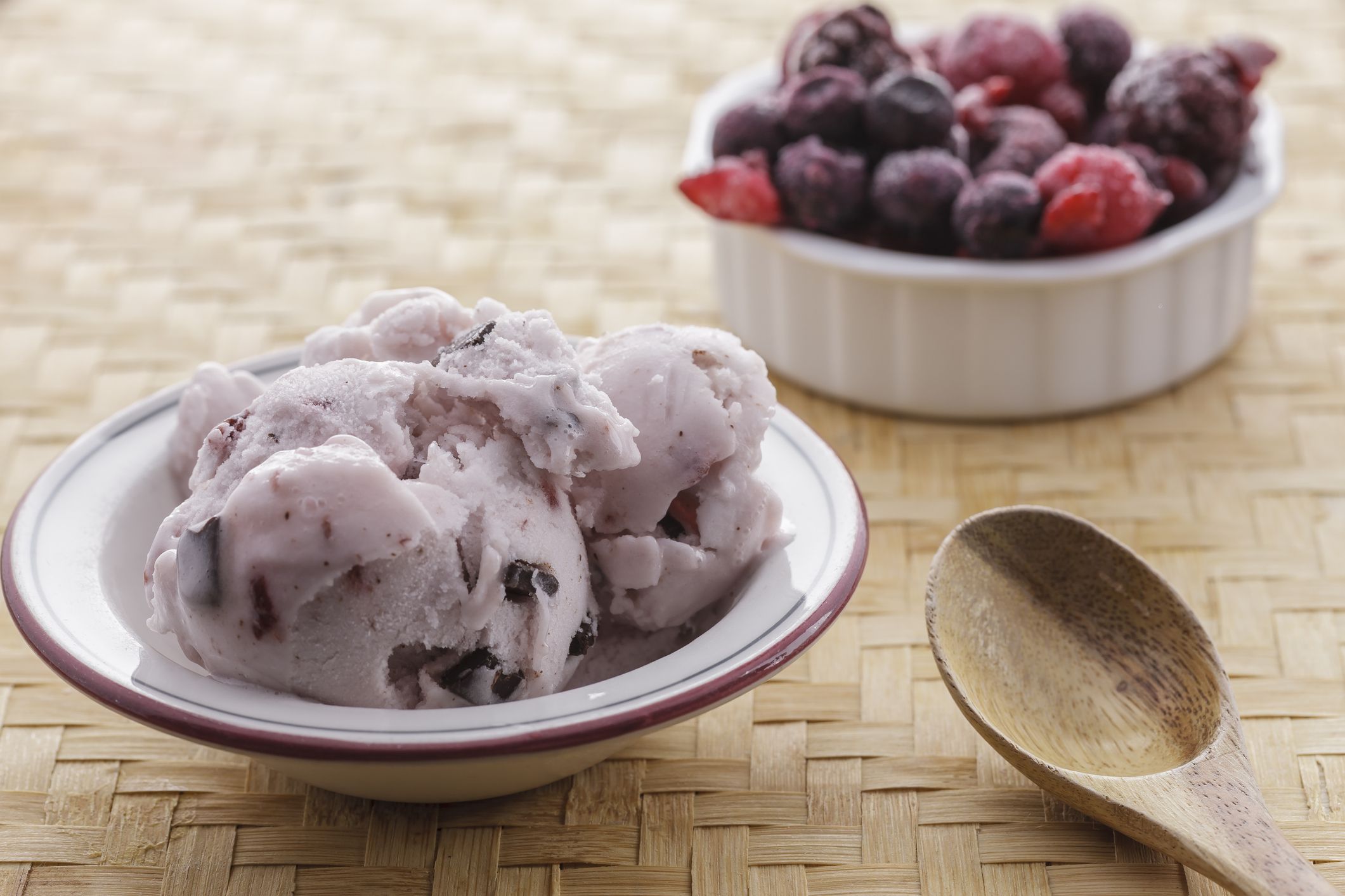 A bowl of cherry chocolate chunk ice cream and a bowl of frozen fruit.