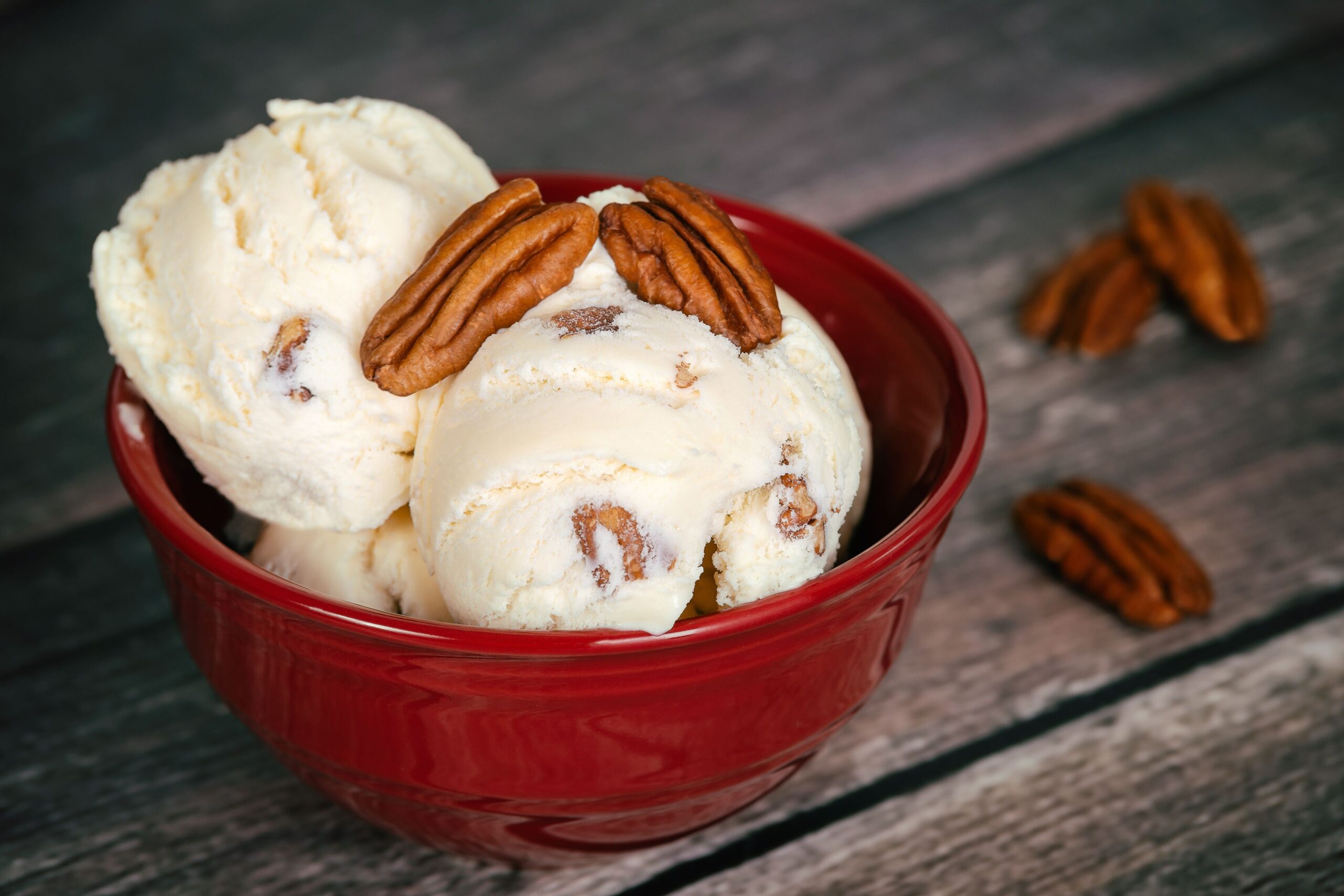 Delicious butter pecan ice cream served in a red bowl. Vintage wooden table background.