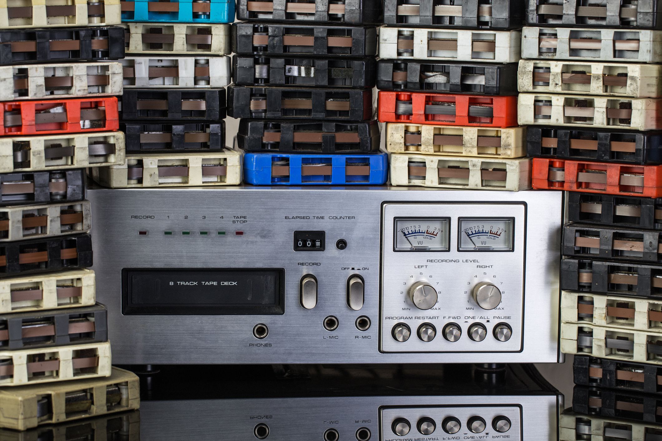 Stacks of 8-track music tapes with a tape deck on a reflective black surface.