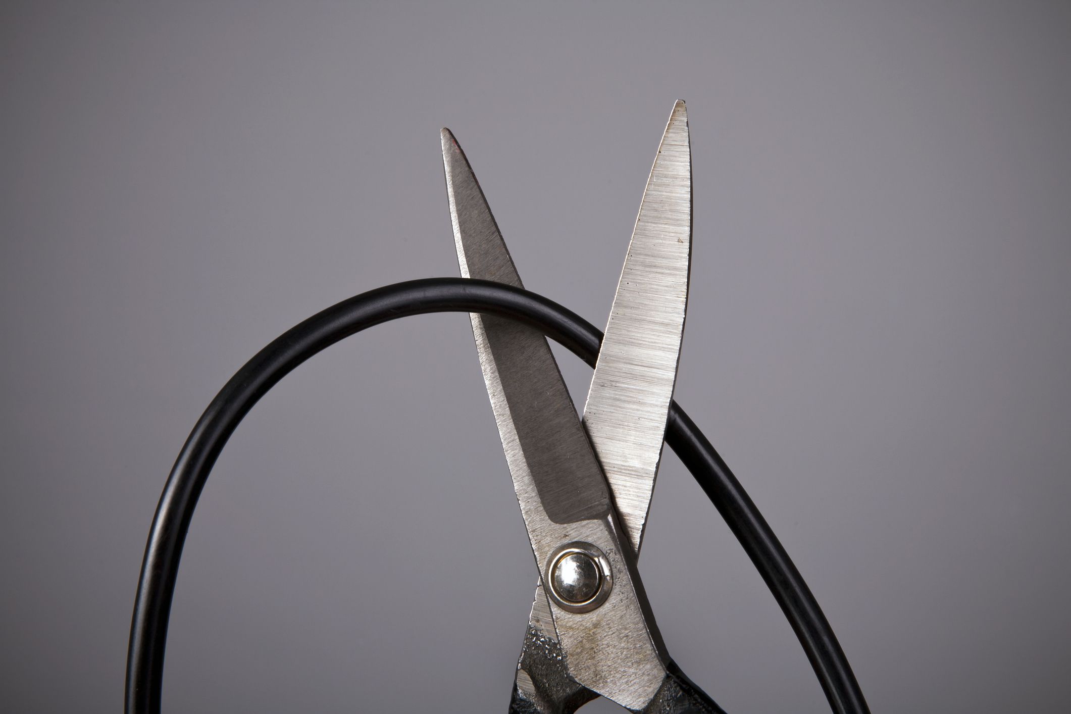 Scissors cutting a computer wire on gray background (wireless or blackout concept)