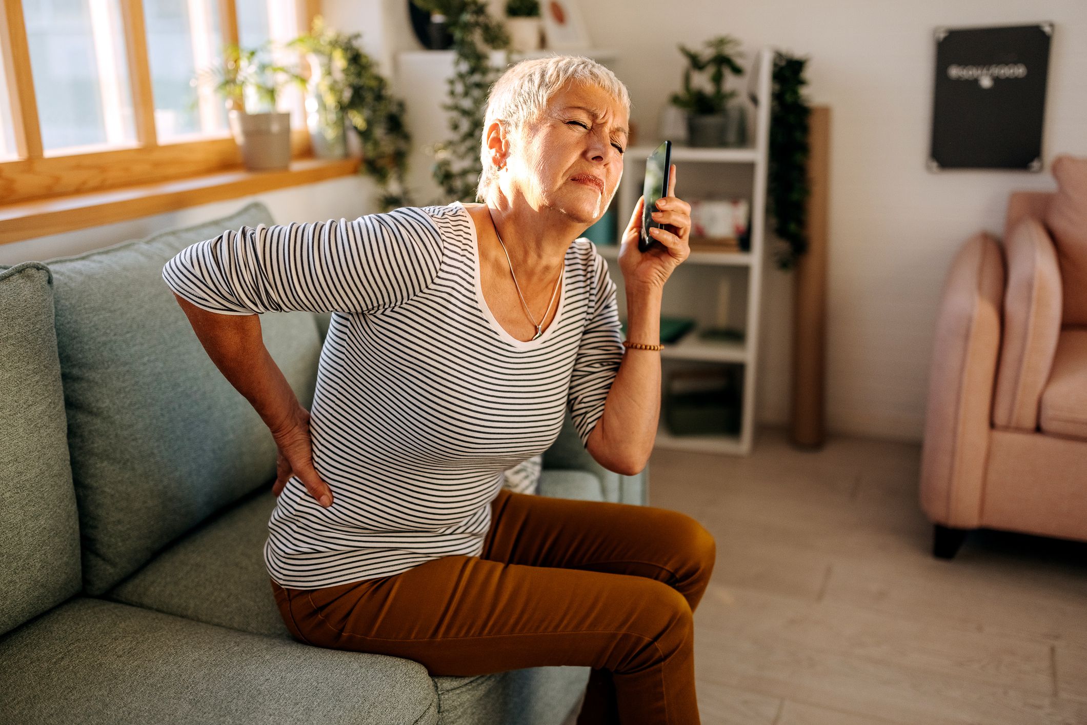 Older woman experiencing back pain, using phone to call ambulance