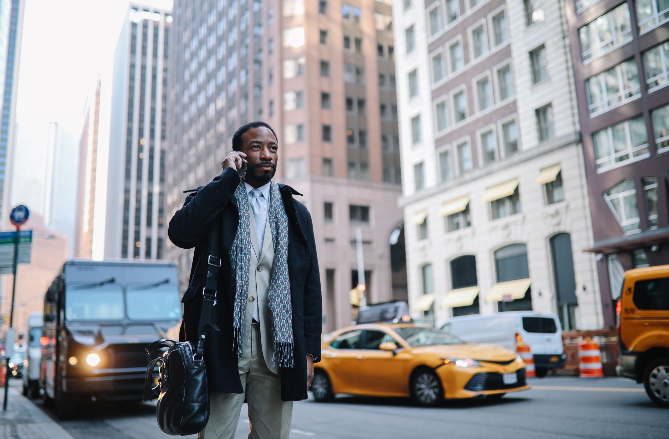 Black mid age businessman walking in NYC downtown, lower Manhattan, getting in or out to his office, wearing a coat and a suit, having a conversation on the phone.