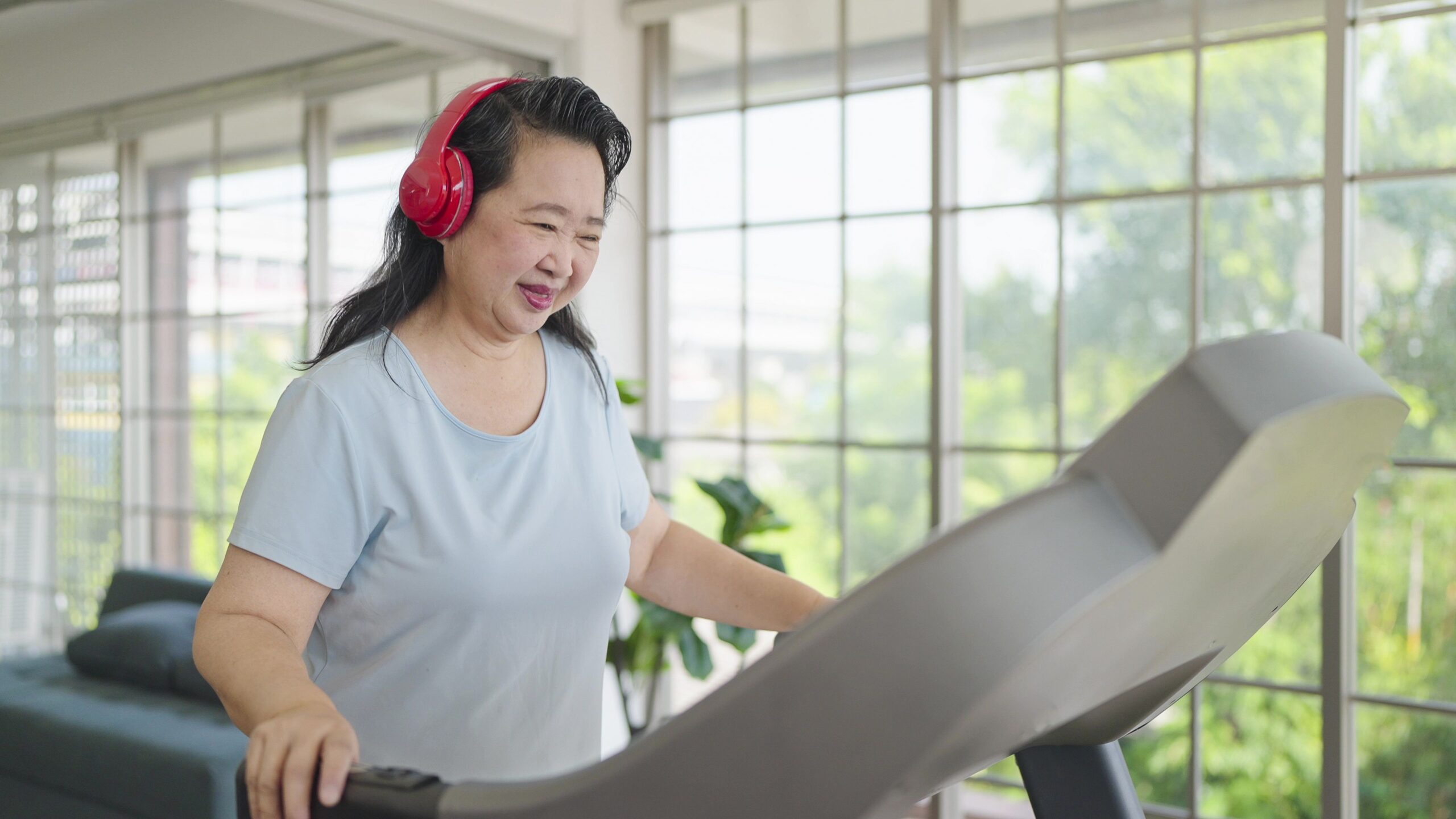 Asian elderly women exercising on the machine in living room at home. Mature woman enjoy doing exercising on treadmill for well being slimming weight. Elderly lifestyle concept