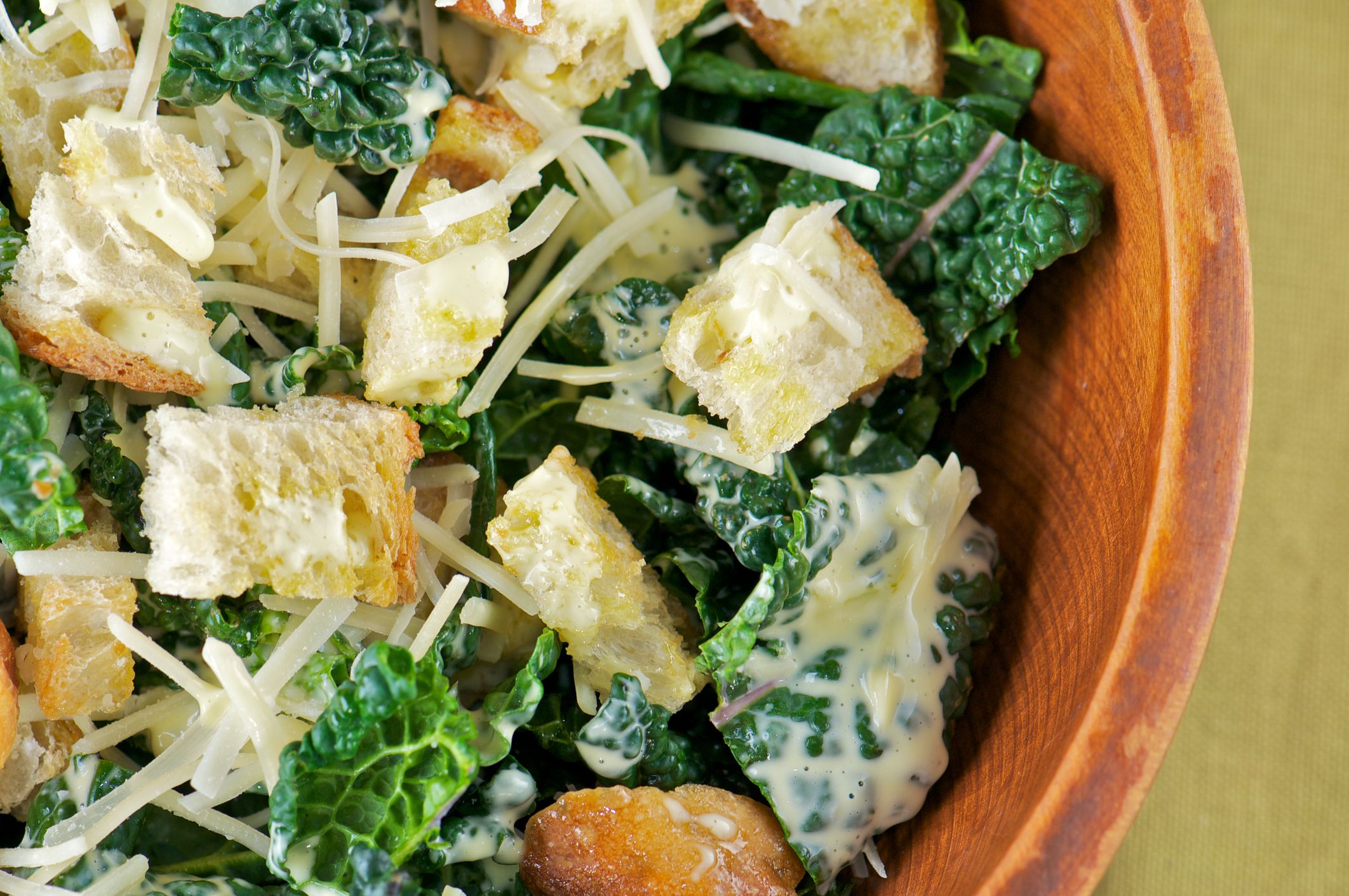 Close-up of kale caesar salad in wooden salad bowl from above
