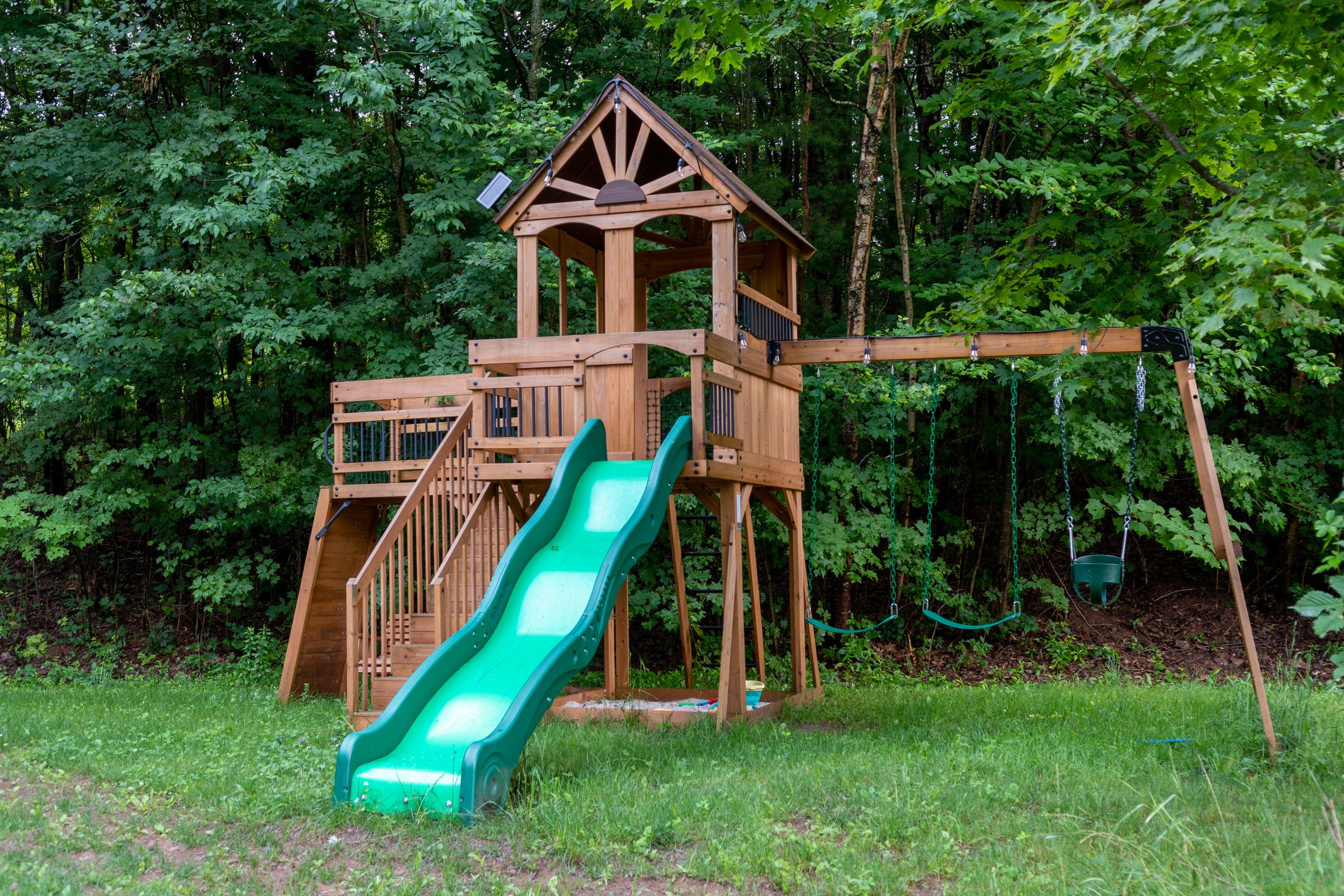 A wooden playground with a green slide and swings in the forest.