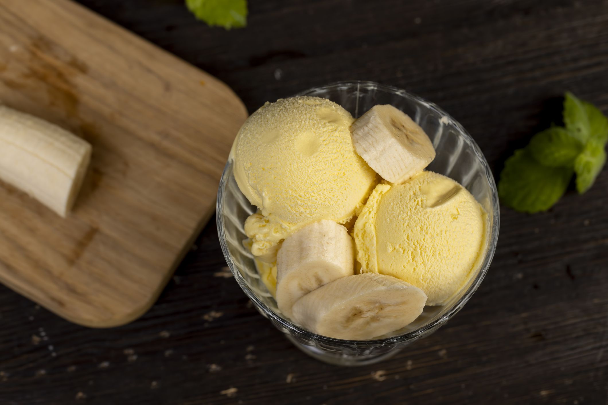sweet ice cream with banana flavor closeup, creamy ice cream with yellow banana slices in a glass cup with mint