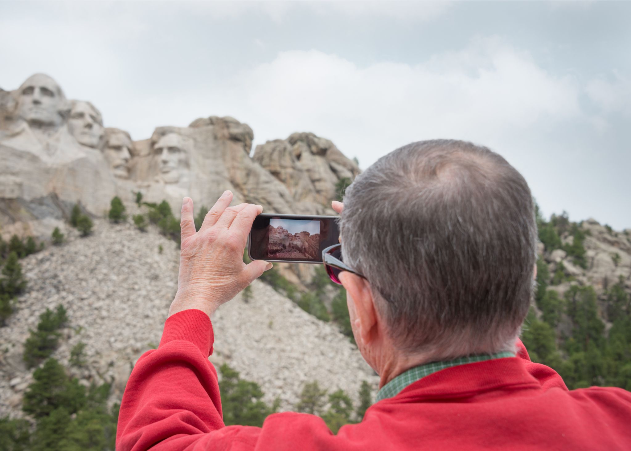 A retired senior man uses modern technology to take a cell phone photo while traveling to Mount Rushmore, South Dakota, USA.