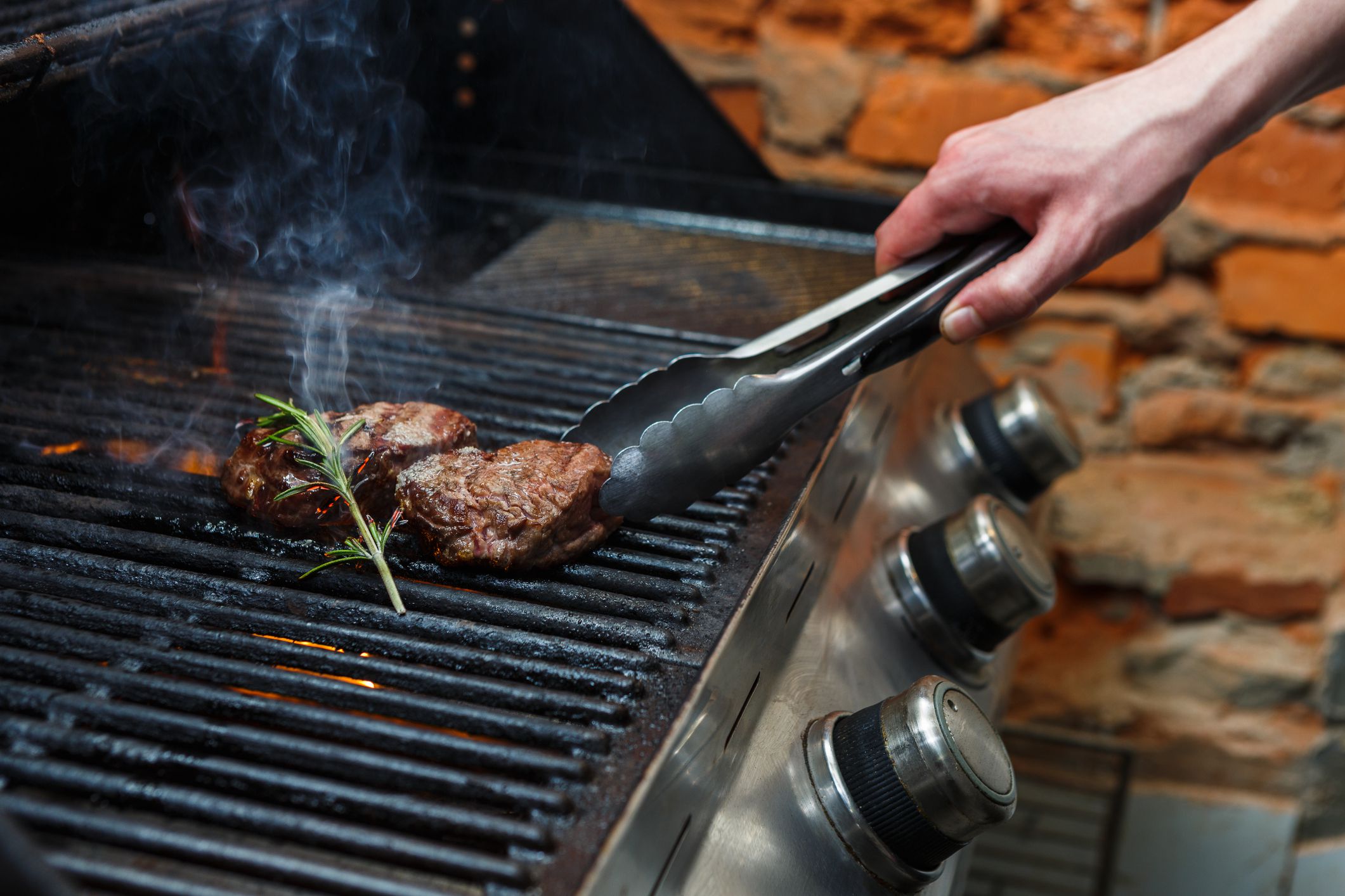 Man cooking meat steaks on professional grill outdoors. Male hand with tongs turning beefsteaks.