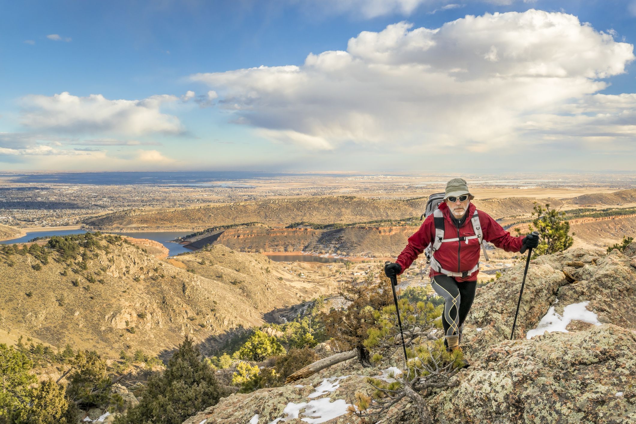a mature backpacker with trekking poles on a mountain ridge in winter scenery - Horsetooth Rock trail above Fort Collins in northern Colorado