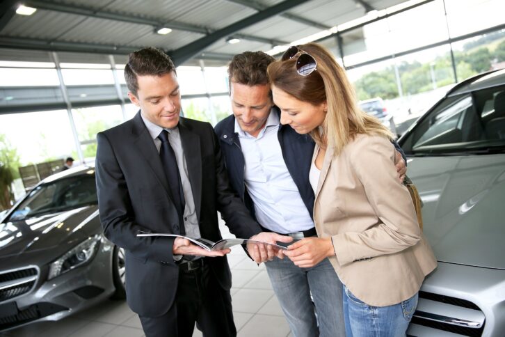 couple in car dealership looking at brochure with salesman