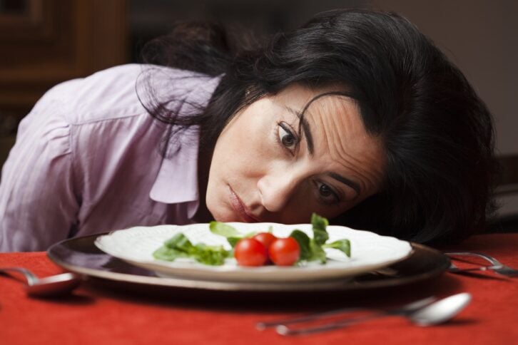 woman looking at three tomatoes on plate