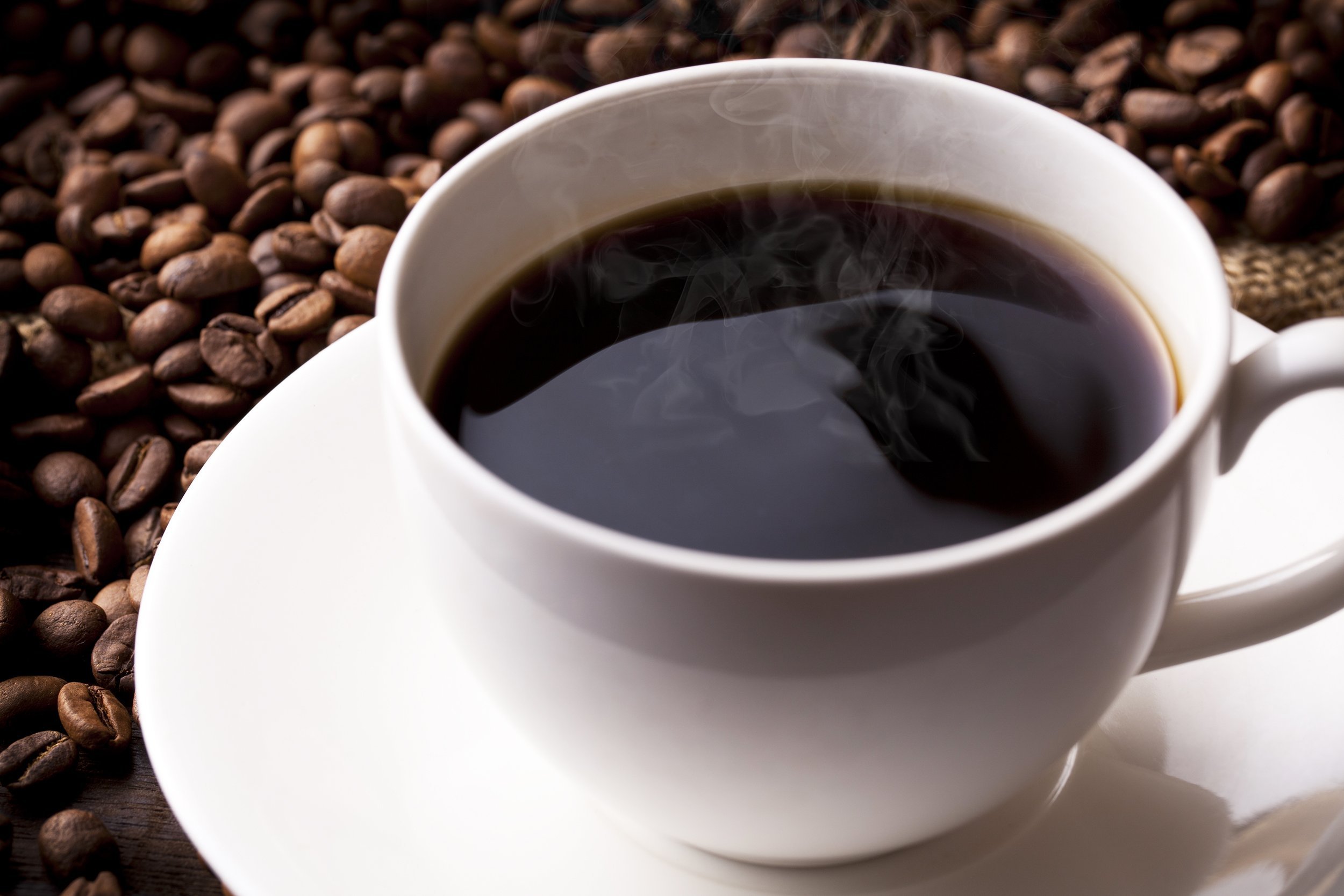 hot coffee in white cup with coffee beans in the background