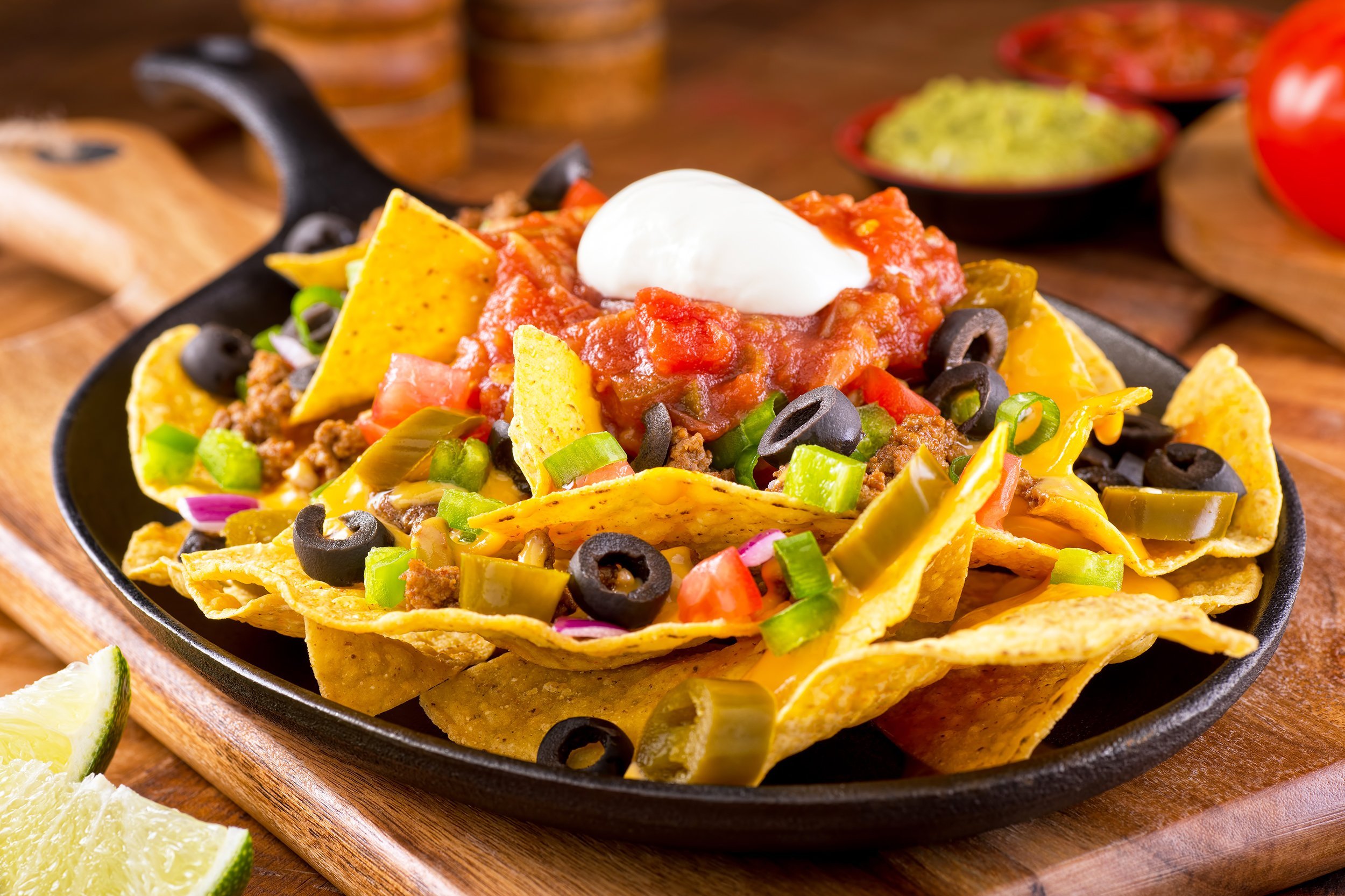 plate of delicious tortilla nachos with melted cheese sauce, ground beef, jalapeno peppers, red onion, green onions, tomato, black olives, salsa, and sour cream