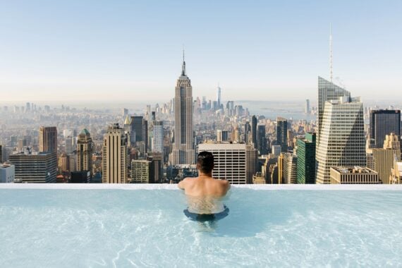 young man relaxing in a swimming pool with view towards New York City skyline