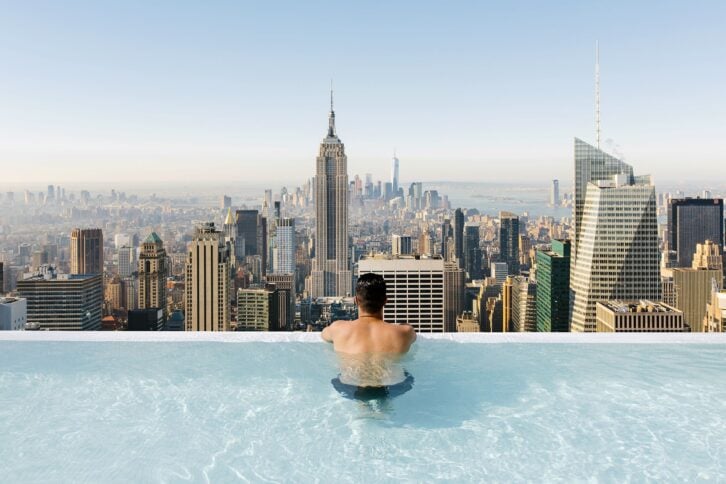 young man relaxing in a swimming pool with view towards New York City skyline