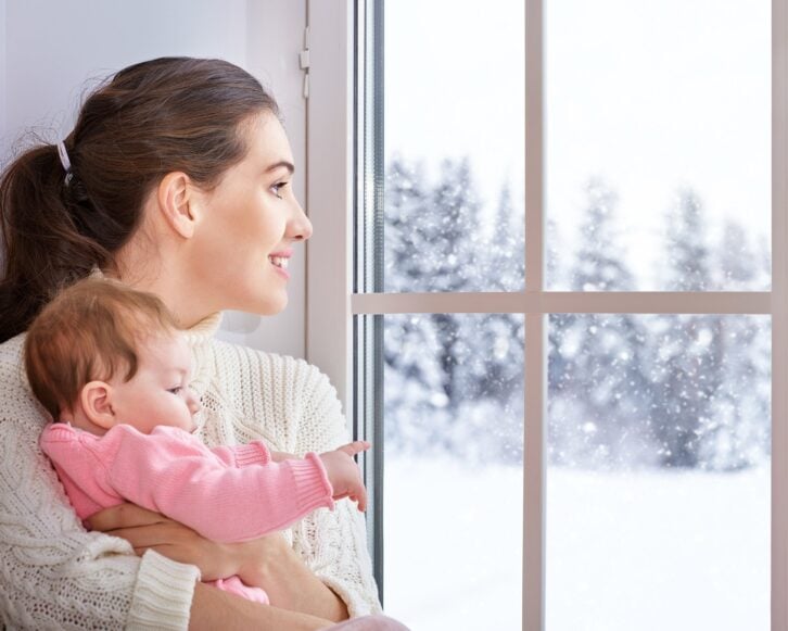 mother and baby hugging near window with snow outside