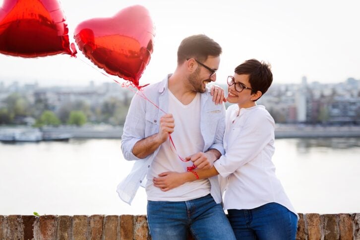 smiling couple in love with heart balloons on sunset