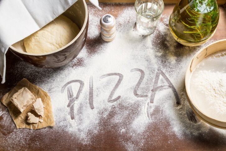 preparing dough for pizza with 'PIZZA' written in dough
