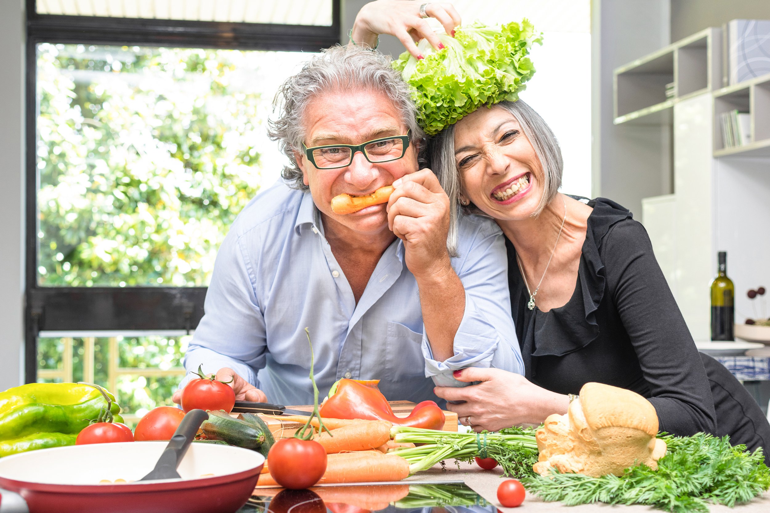senior couple having fun in kitchen cooking healthy food together