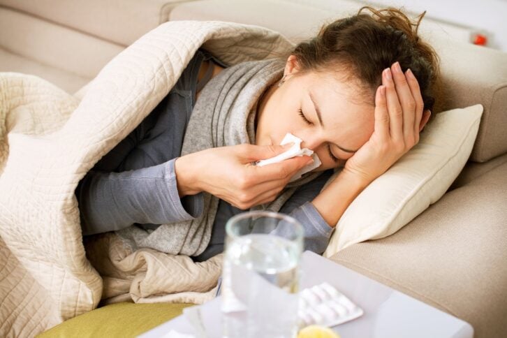 sick woman sneezing into tissue while in bed