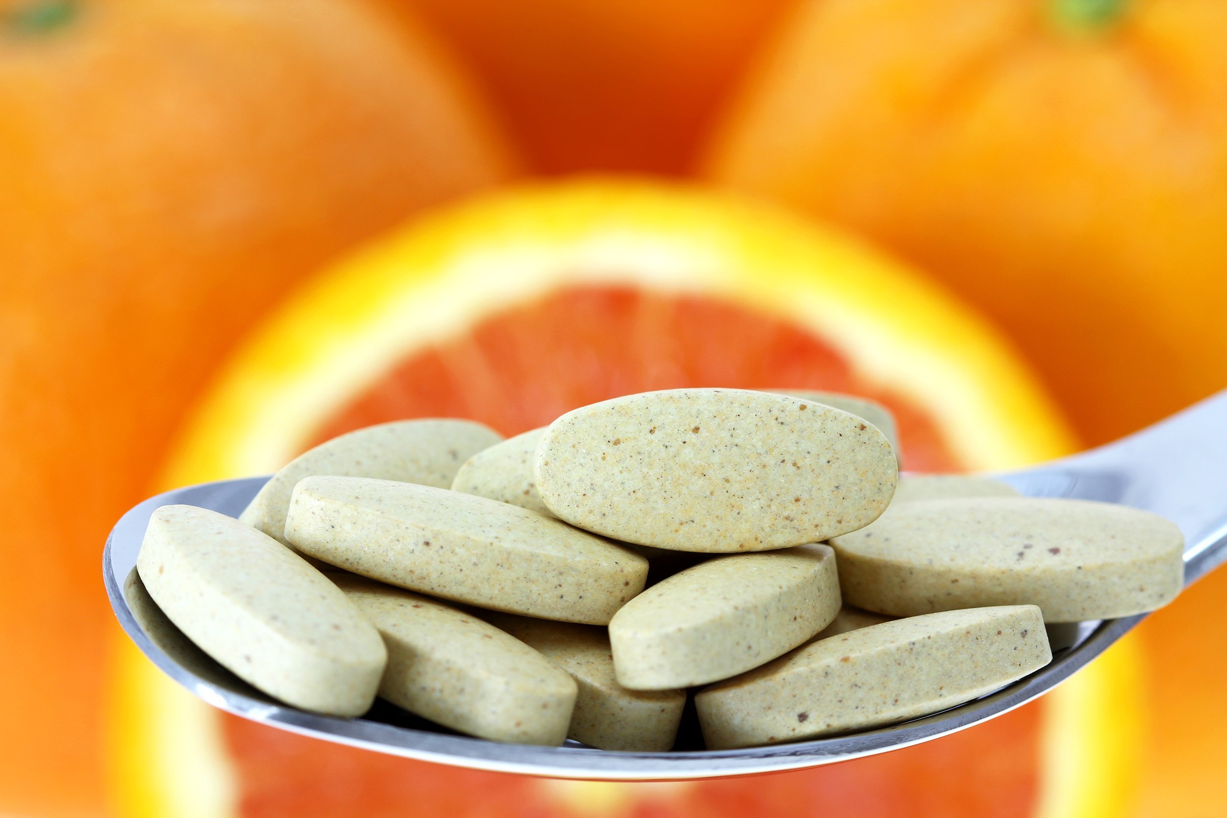 spoon of Vitamin C tablets with blurred background of fresh orange