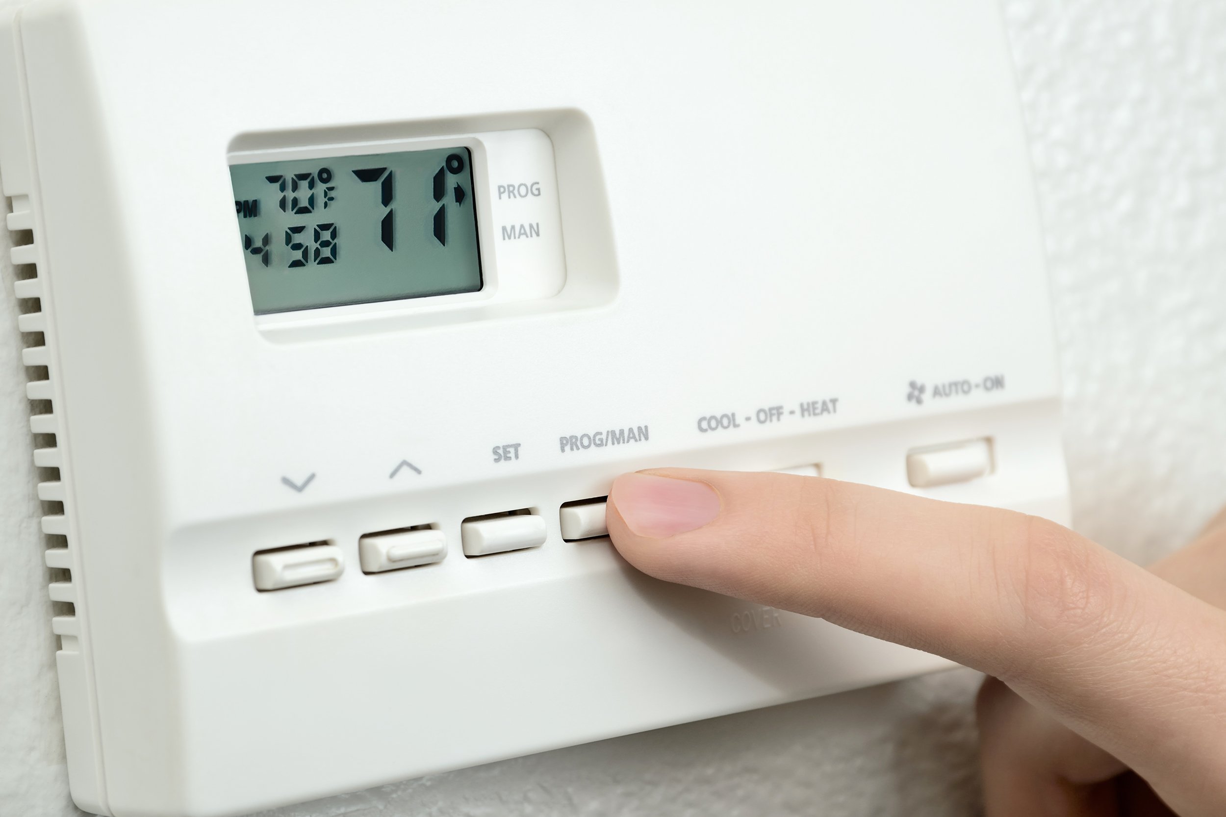 finger pressing button on digital thermostat